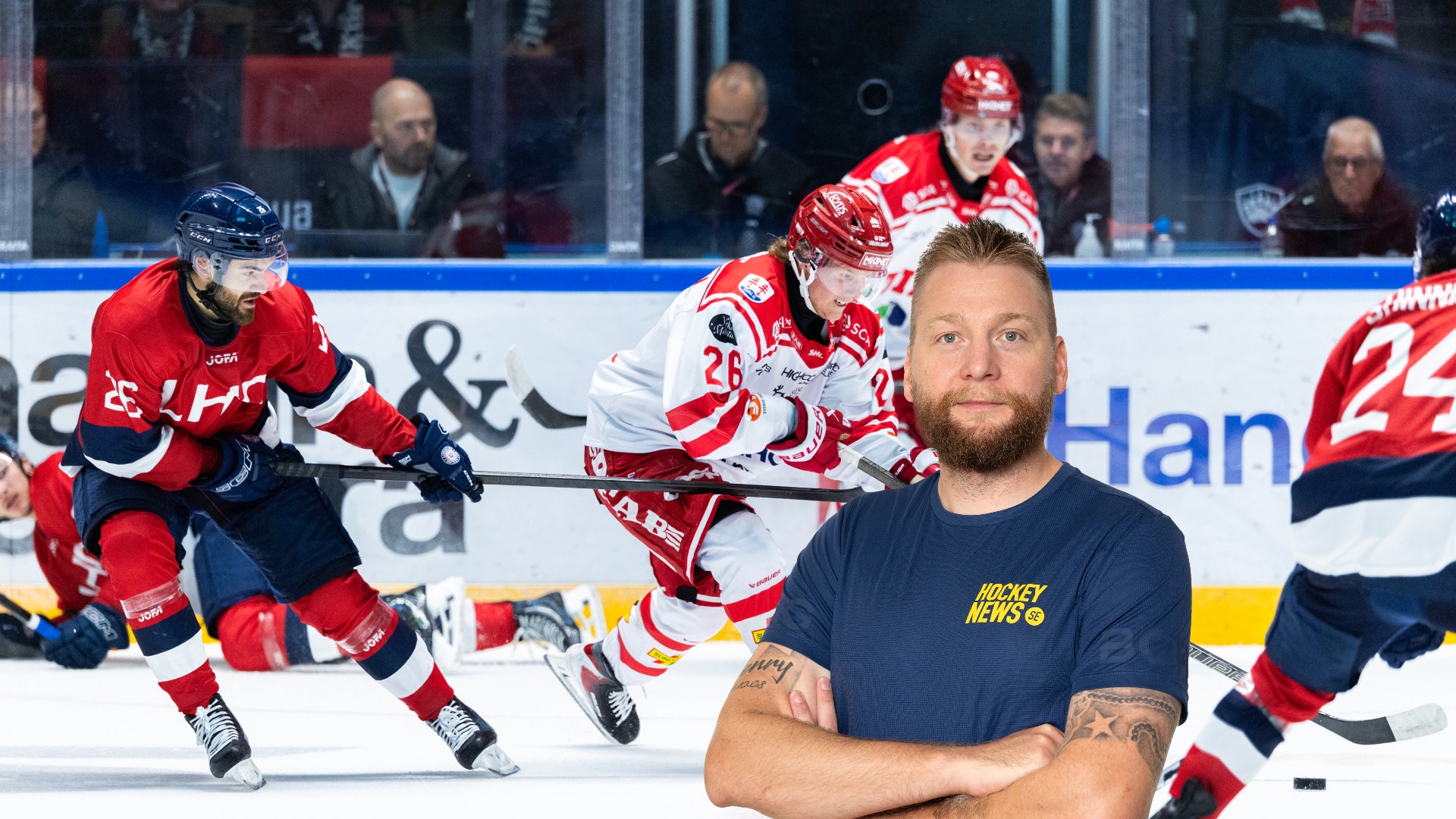 En man med skägg står med armarna korsade framför en ishockeyplan där spelare i röda och blåa matchtröjor spelar match.