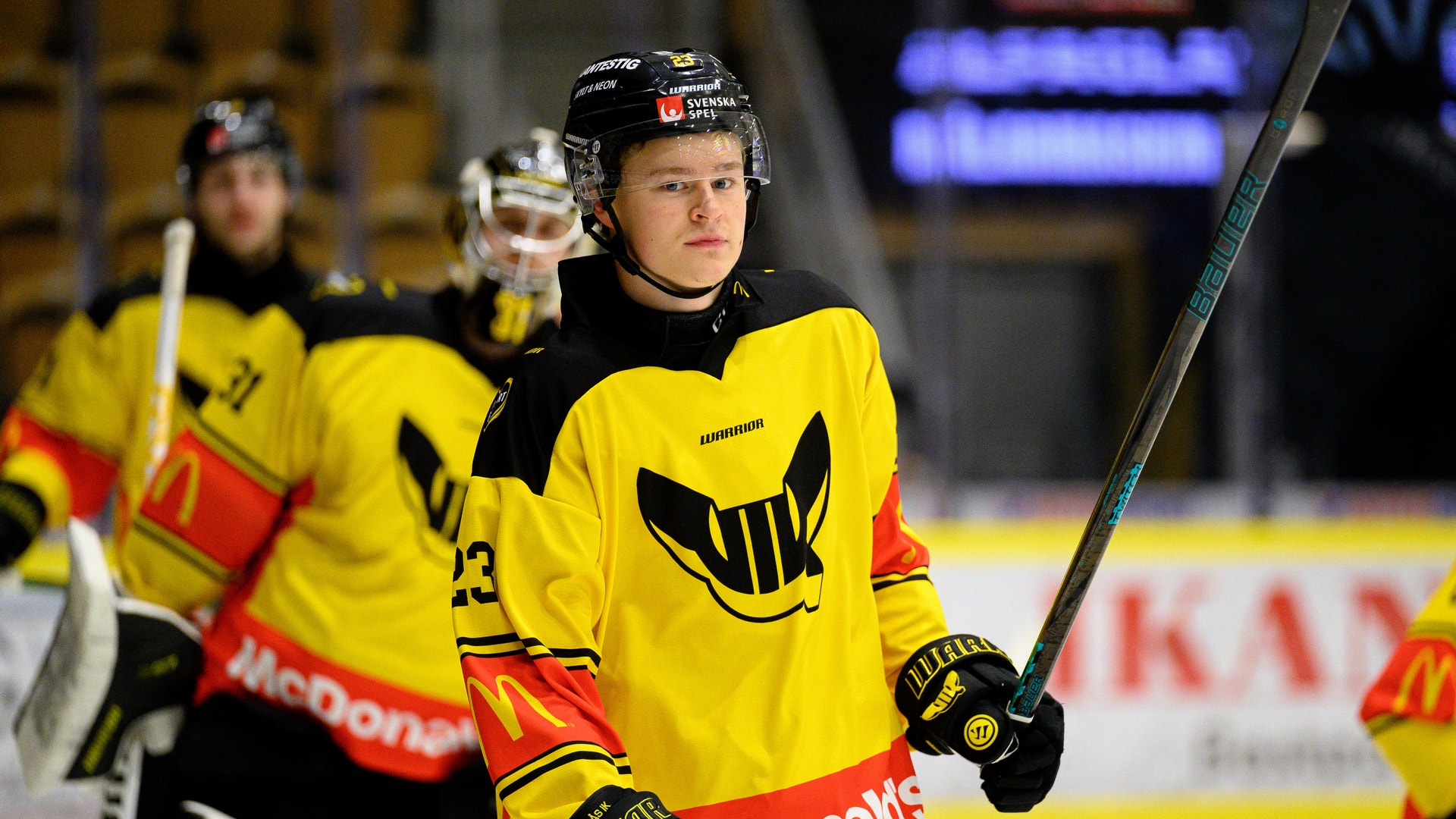 Ishockeyspelare i gul och svart tröja med hockeyklubbe under en match på isen.