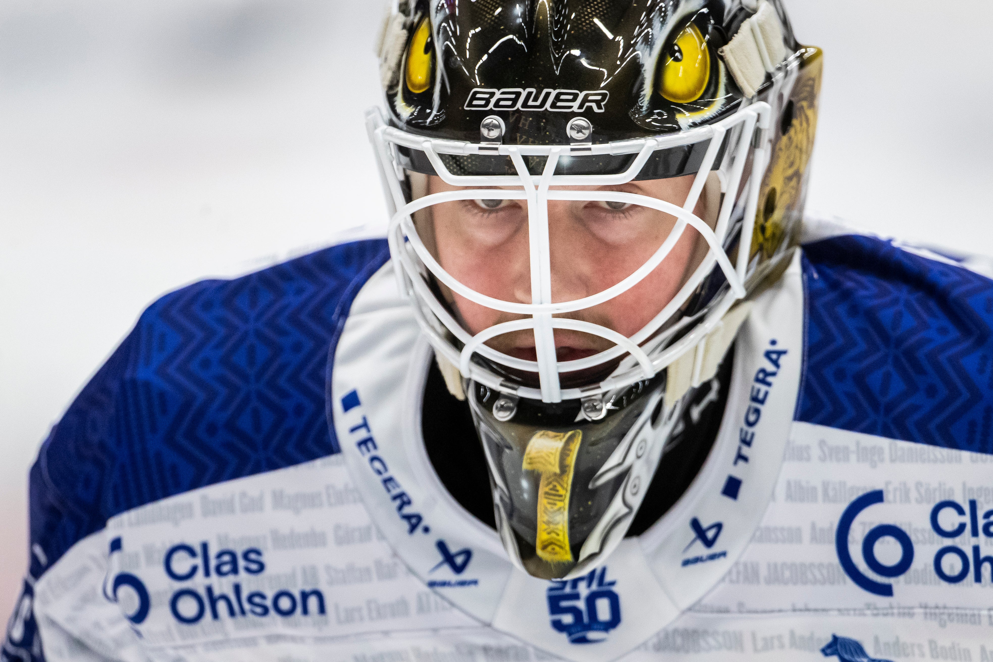 Porträtt av en ishockeysmålvakt i blå och vit uniform med skyddsutrustning och ansiktsmask.