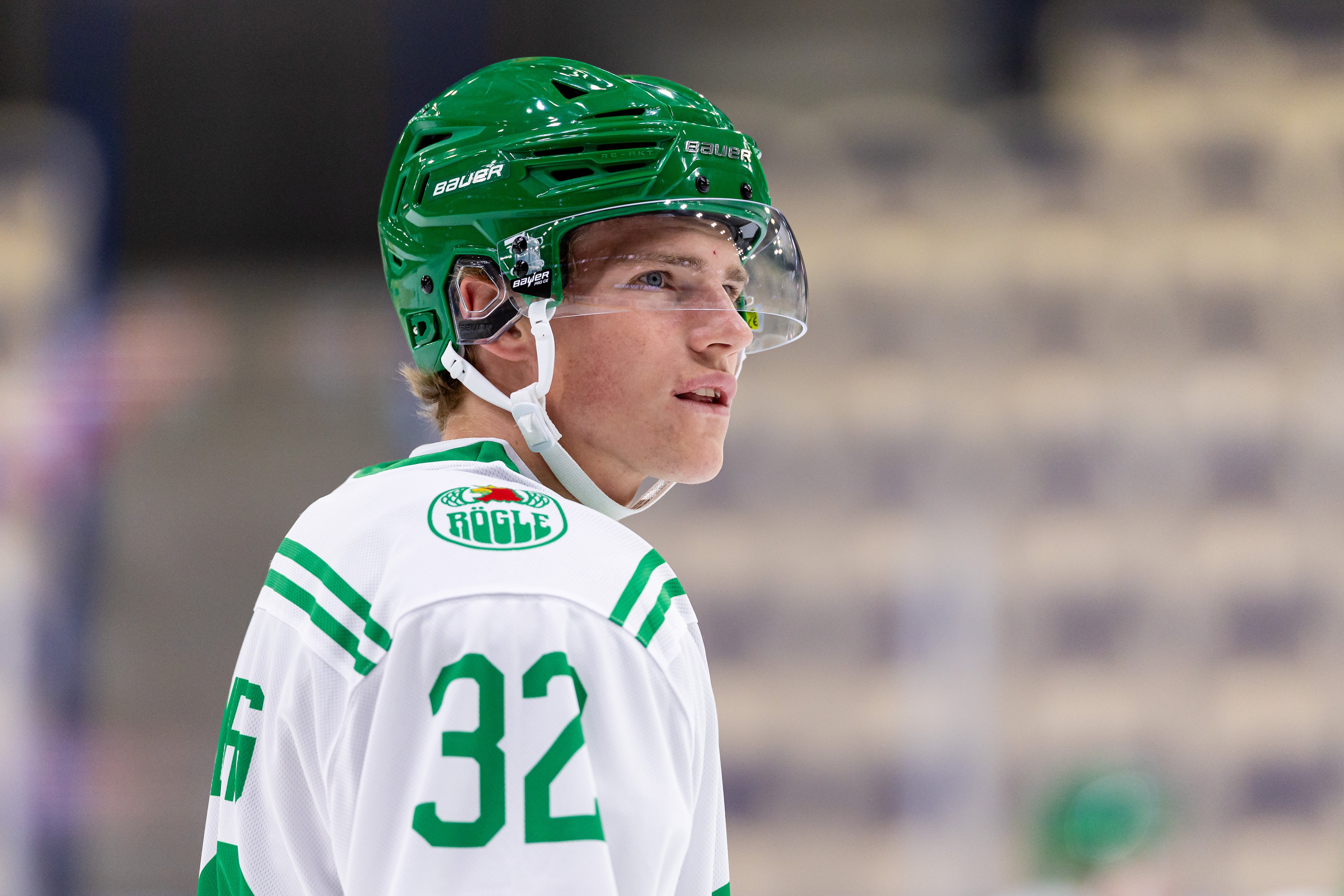 Ishockeyspelare i vit och grön tröja med nummer 32 bär en grön hjälm med visir under en match.