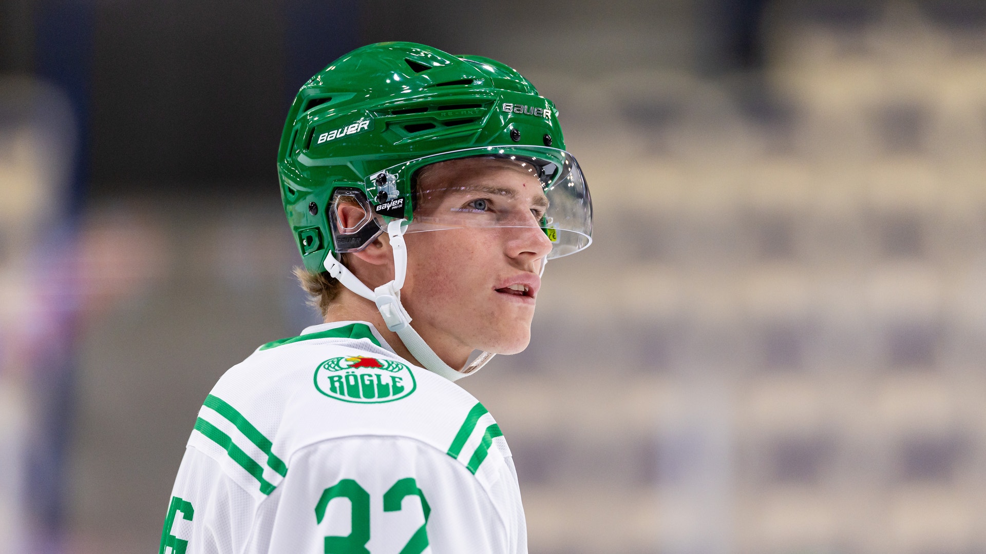 Ishockeyspelare i vit och grön tröja med nummer 32 bär en grön hjälm med visir under en match.