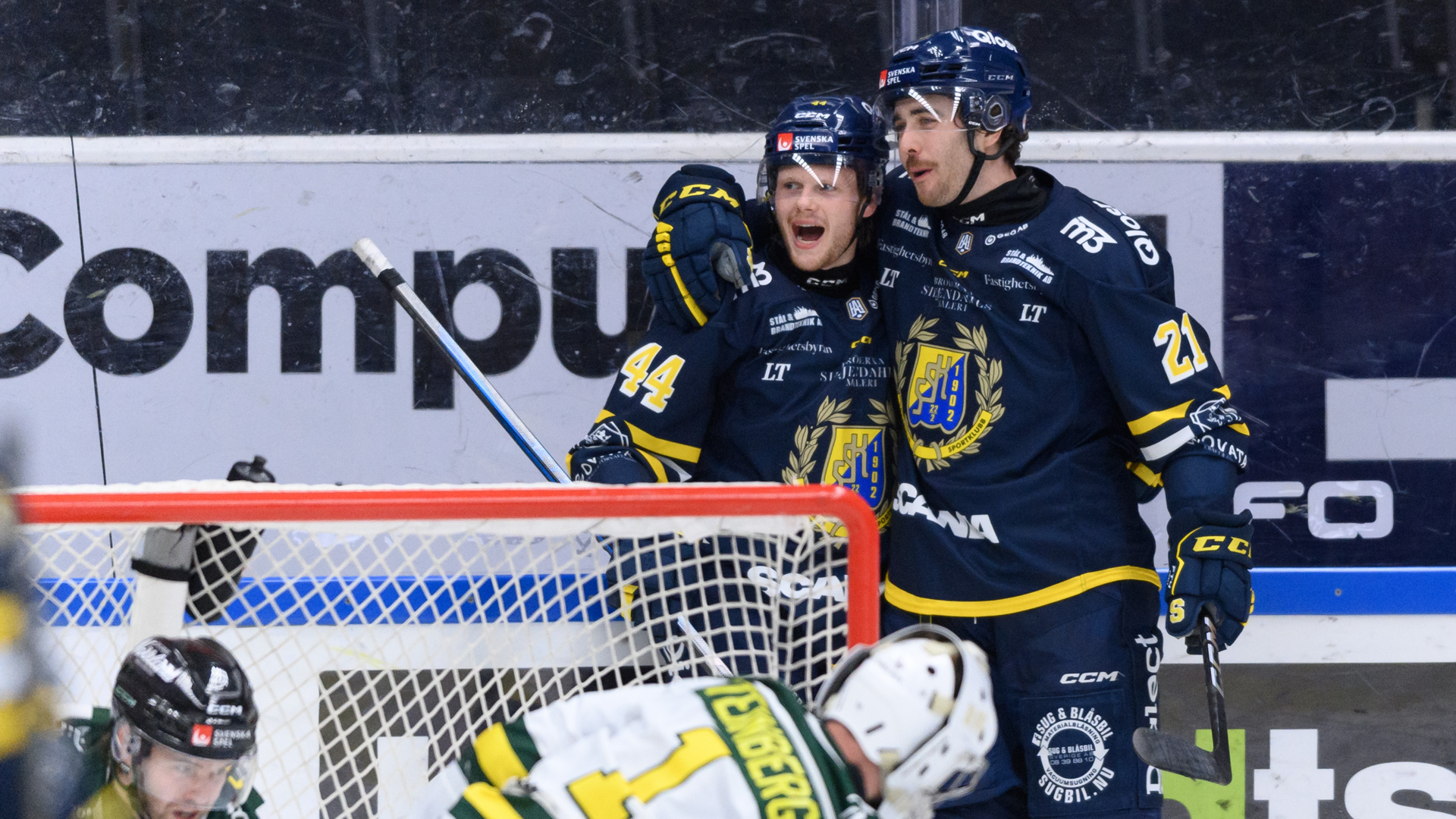 Två hockeyspelare i blå och gula tröjor jublar framför målet under en match.