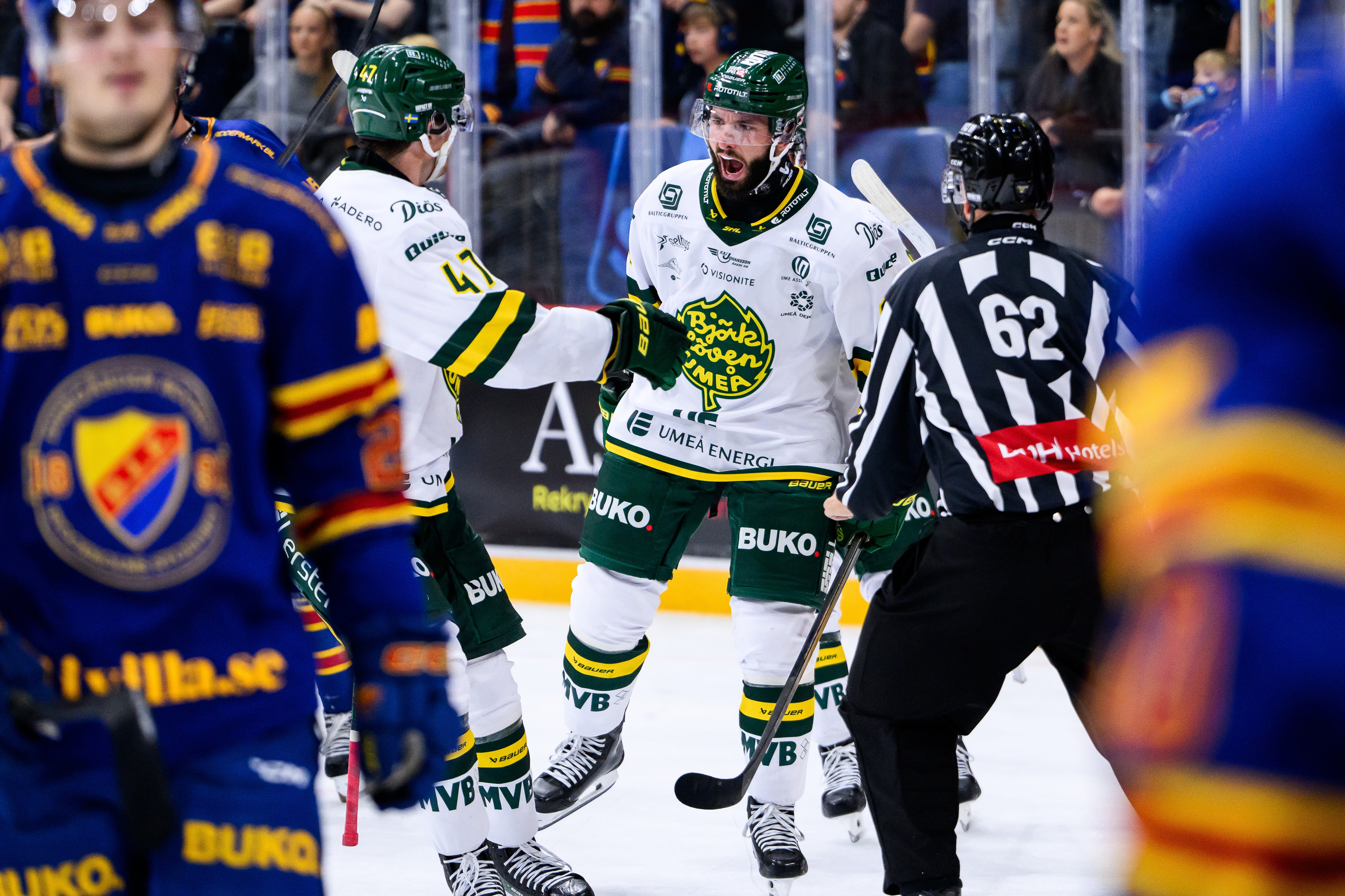 Ishockeyspelare i vita matchtröjor jublar tillsammans på isen, med en domare i randig tröja i närheten.