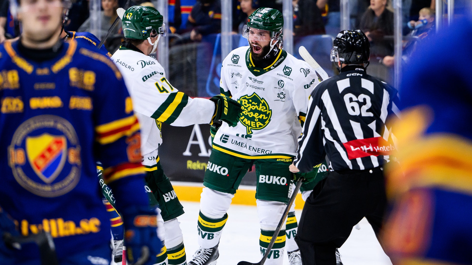 Ishockeyspelare i vita matchtröjor jublar tillsammans på isen, med en domare i randig tröja i närheten.