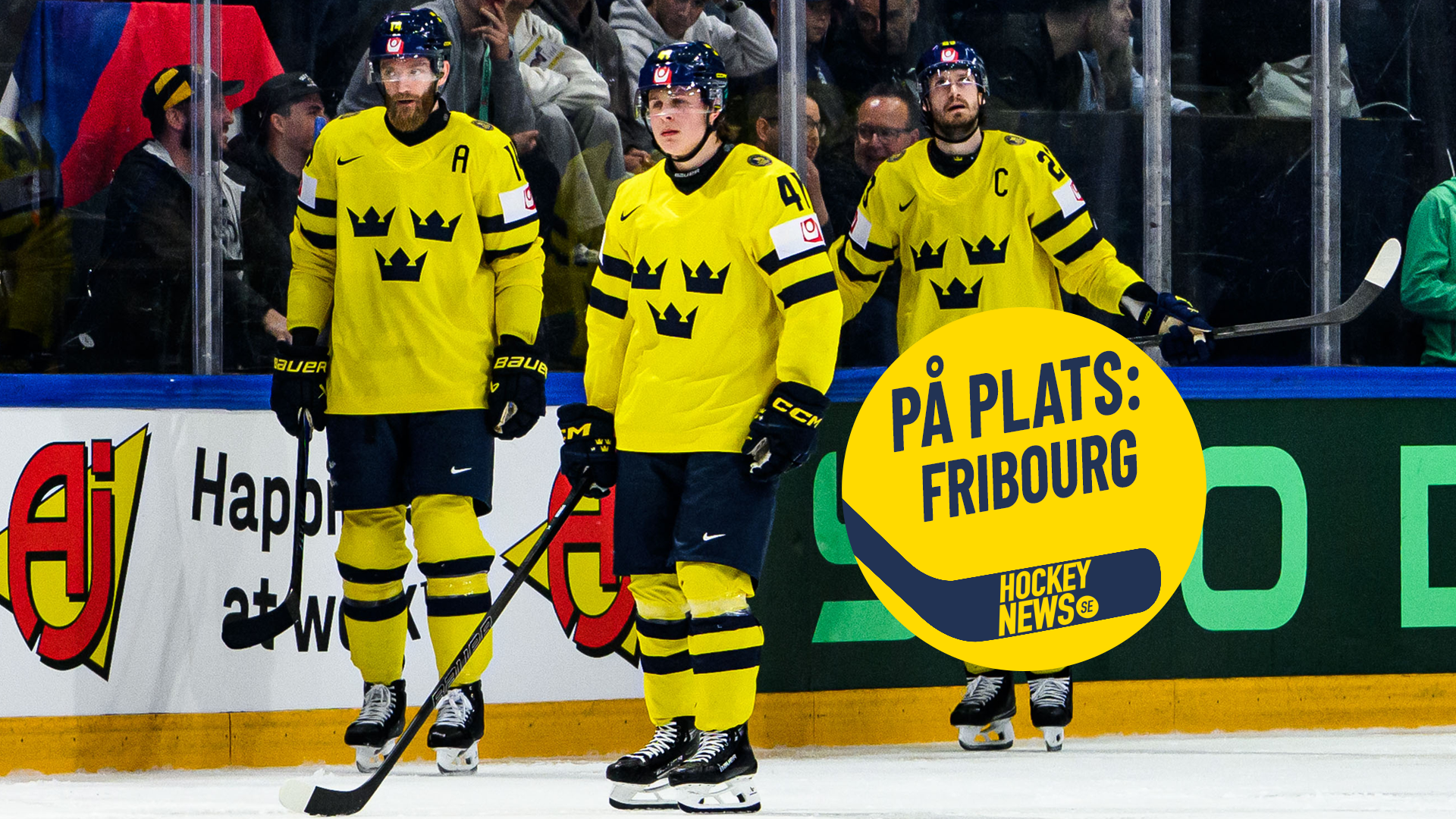 Tre ishockeyspelare i gula och svarta landslagströjor går på isen under en match. Tre ishockeyspelare i gula och svarta landslagströjor går på isen under en match. Publiken och bandbyten syns i bakgrunden.