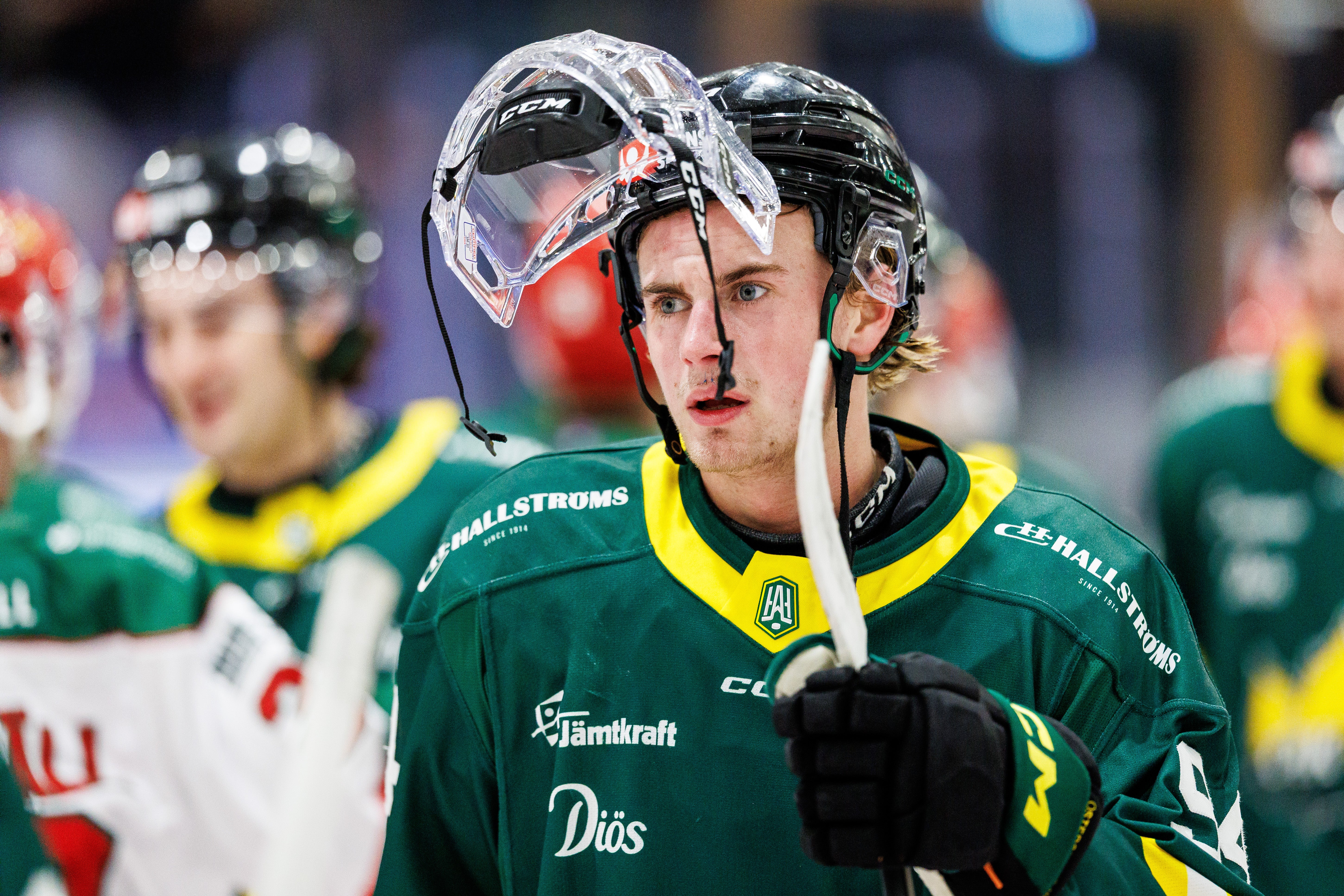 Ishockeyspelare i grön och gul uniform med hjälm och stick under en match.