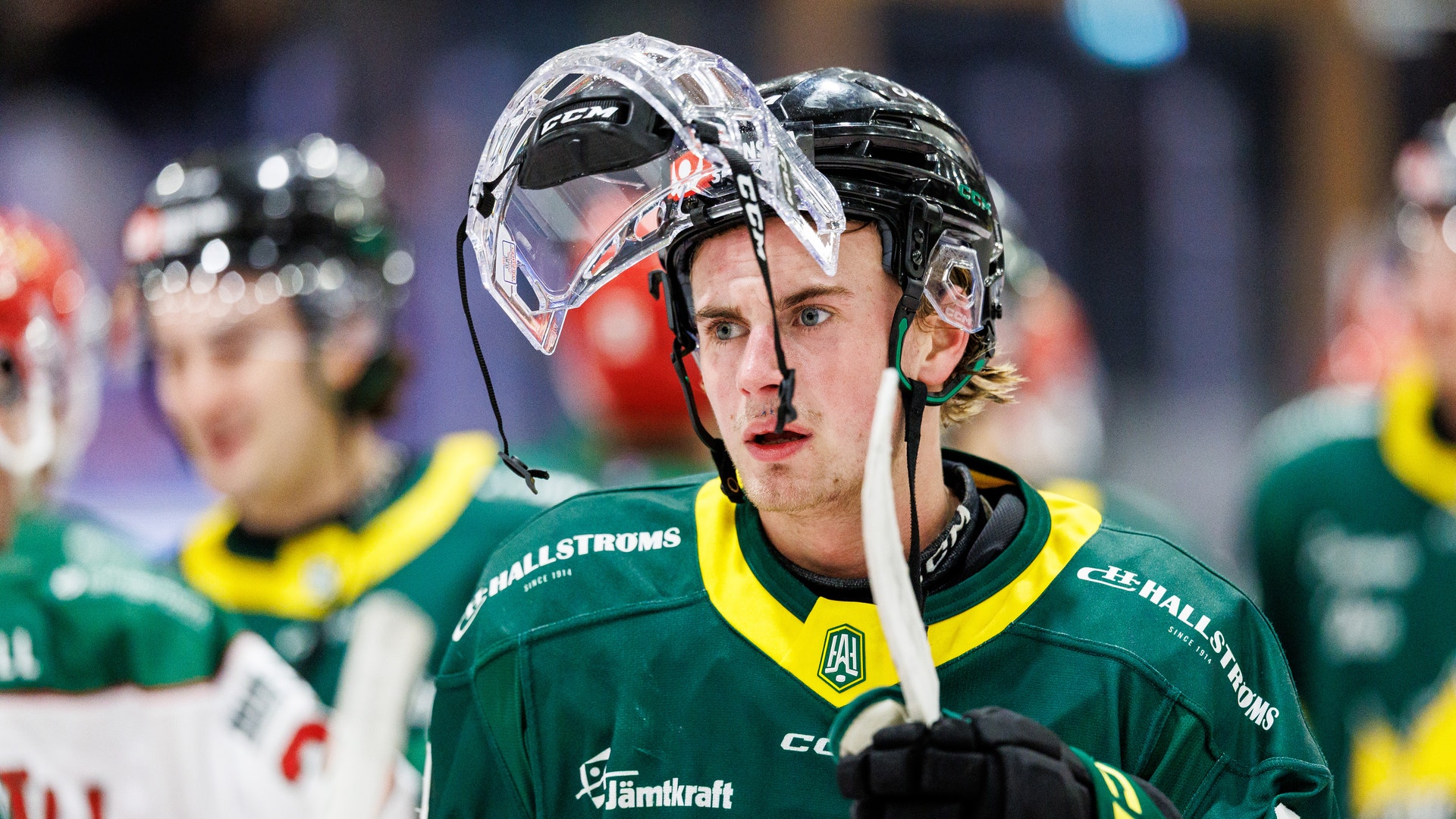 Ishockeyspelare i grön och gul uniform med hjälm och stick under en match.