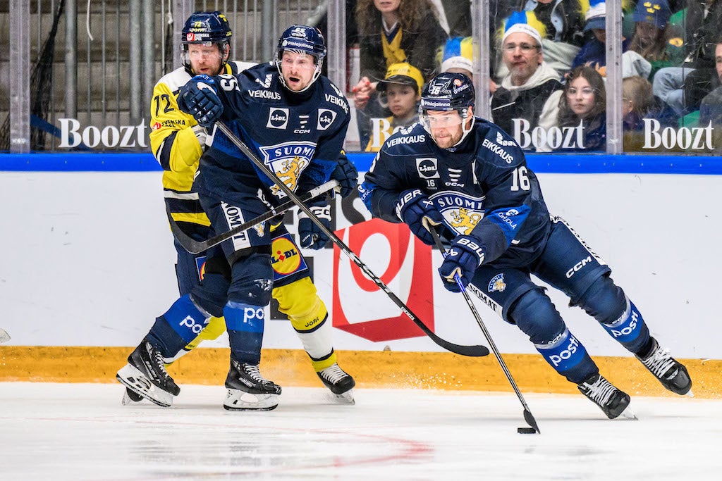 Ishockeymatch där spelare från två lag kämpar om pucken på isen. En spelare i mörkblå och gul tröja försöker ta pucken från en motspelare i mörkblå tröja. Publik och bandreklamering syns i bakgrunden.