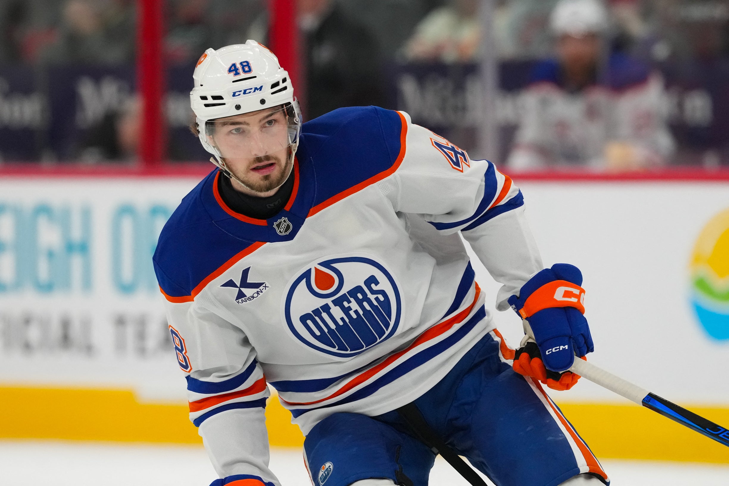 Ishockeyspelare i Edmonton Oilers vita tröja under en match. Spelaren är i rörelse på isen med fokuserad blick.
