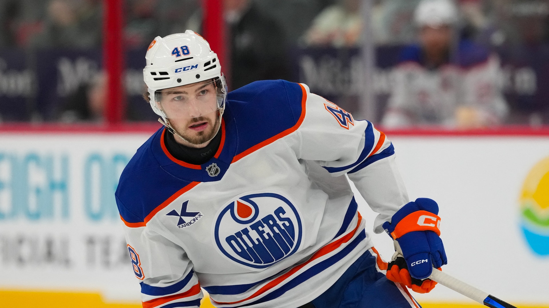 Ishockeyspelare i Edmonton Oilers vita tröja under en match. Spelaren är i rörelse på isen med fokuserad blick.