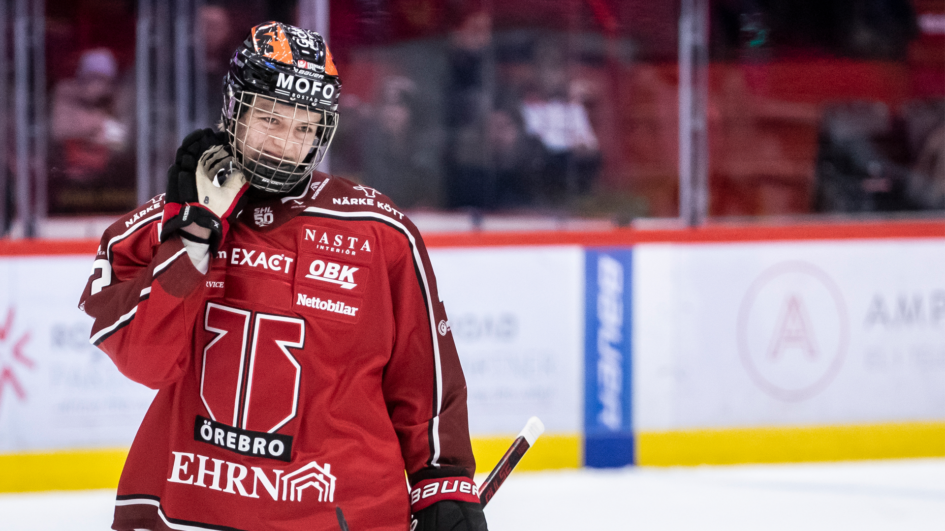 En ishockeyspelare i röd matchdräkt justerar sin hjälm under en ishockeymatch på isen.