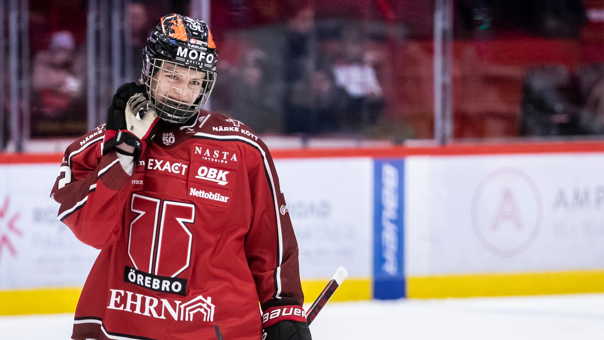 En ishockeyspelare i röd matchdräkt justerar sin hjälm under en ishockeymatch på isen.