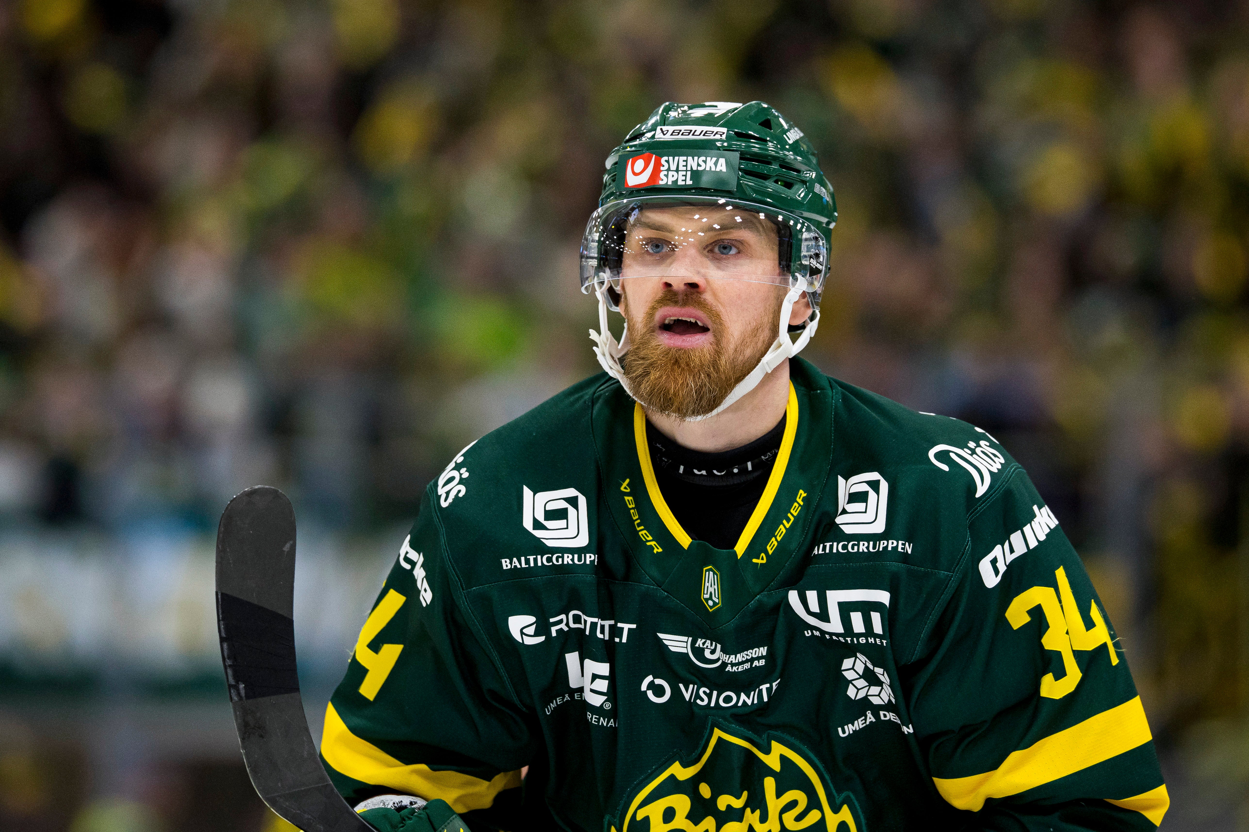 Ishockeyspelare i grön och gul matchdräkt med hjälm under en ishockeymatch.