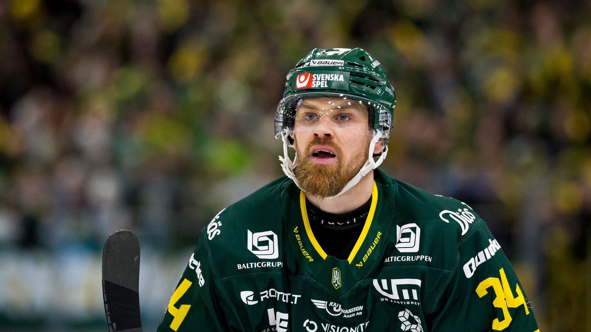 Ishockeyspelare i grön och gul matchdräkt med hjälm under en ishockeymatch.