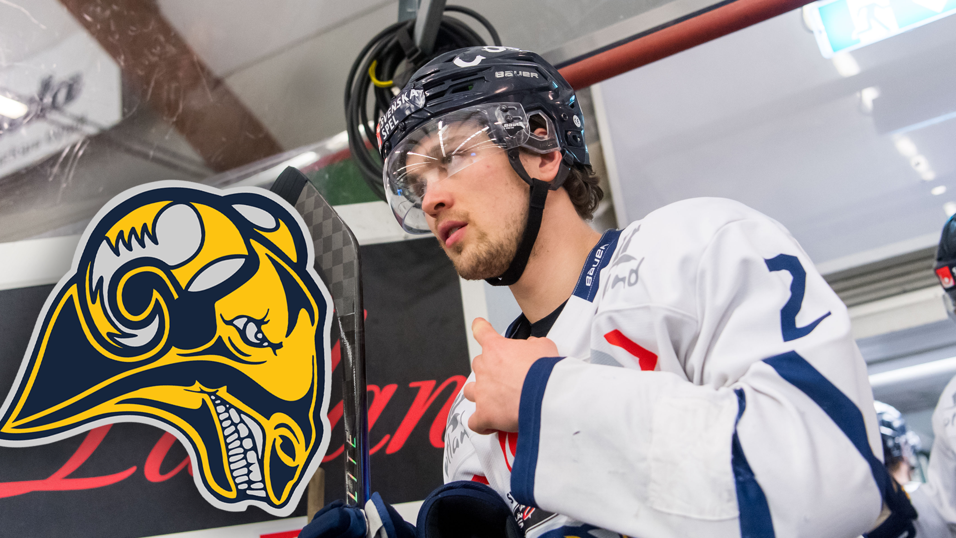 Ishockeyspelare i vit tröja med nummer 2 står bredvid lagbänken under match eller träning.