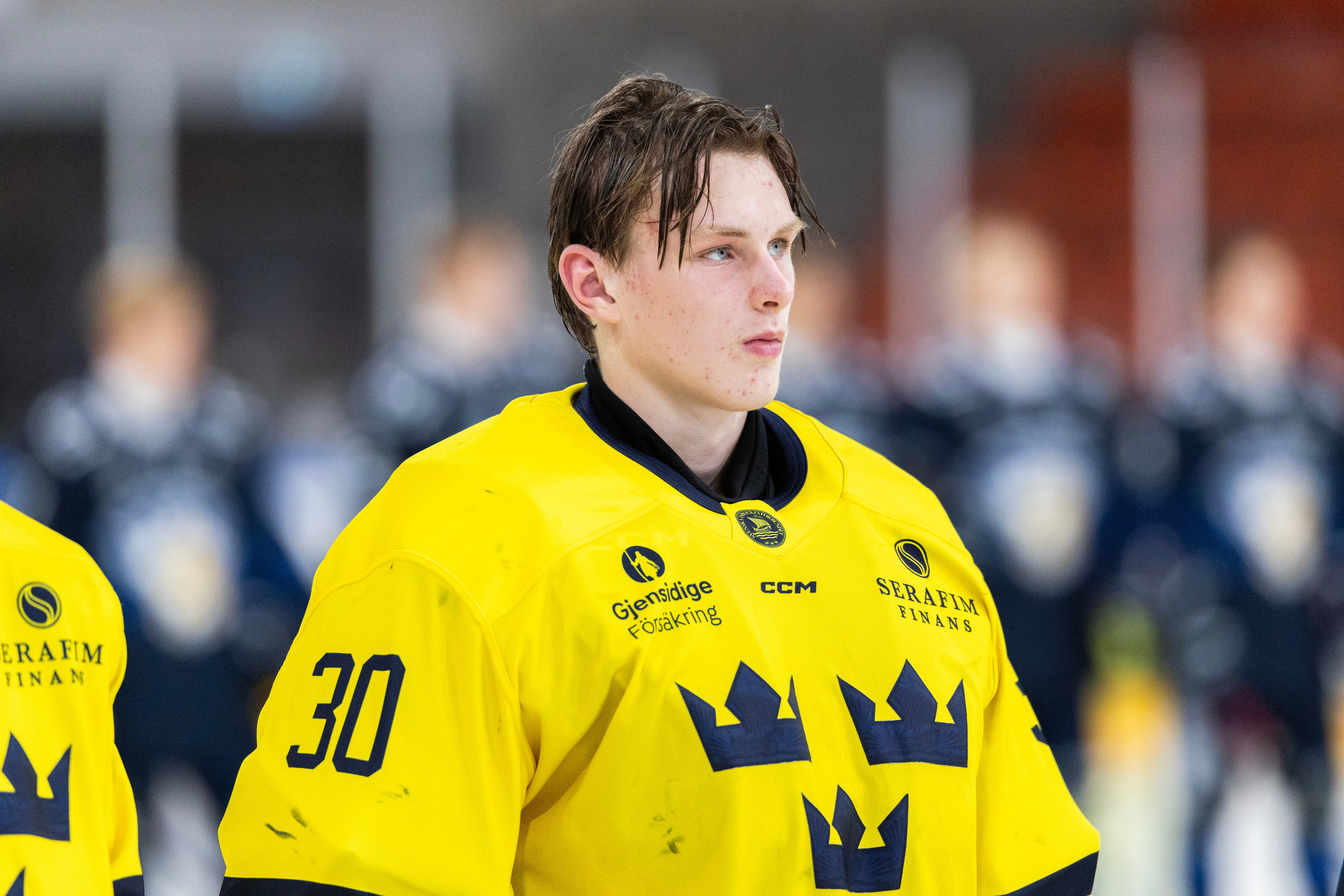 Ishockeyspelare i gul svensk landslagströja med nummer 30 och tre kronor-märket, står på isen under en match.
