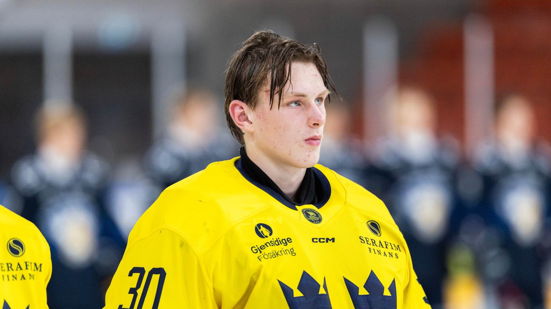 Ishockeyspelare i gul svensk landslagströja med nummer 30 och tre kronor-märket, står på isen under en match.