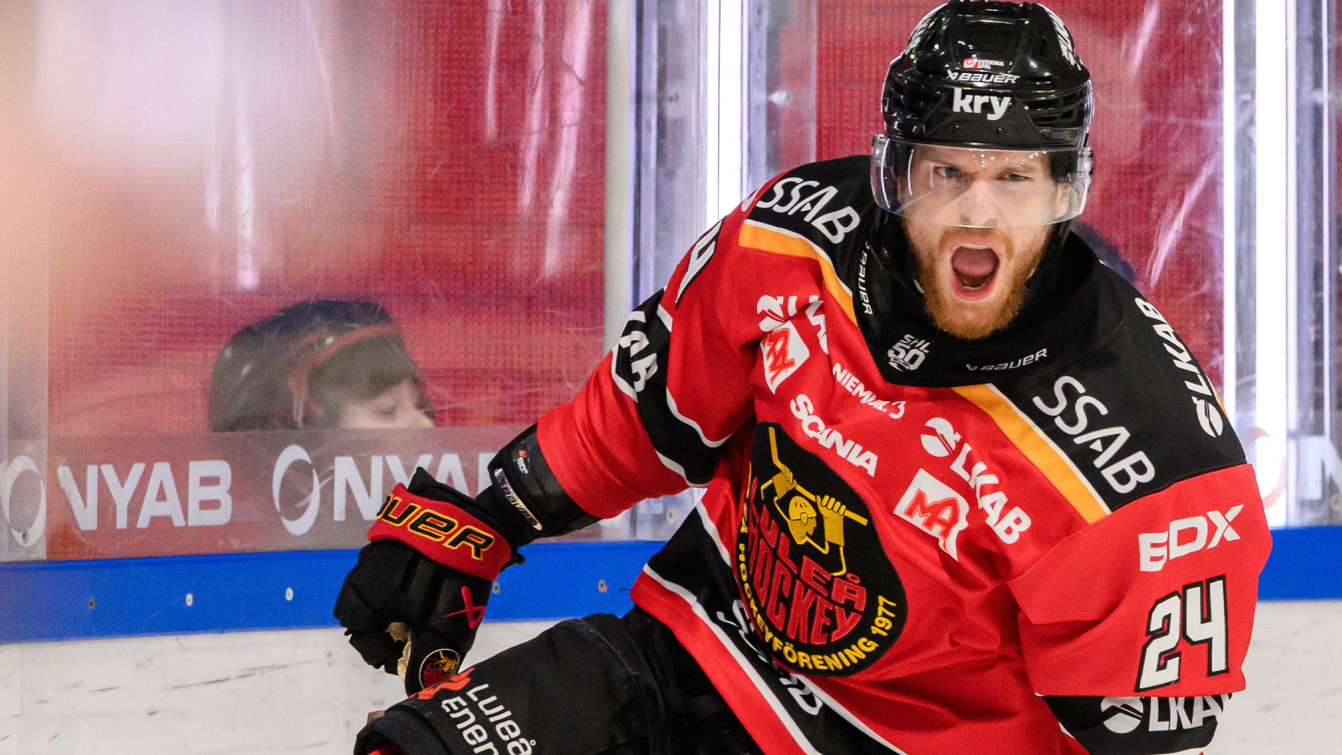 Hockeyspelare i röd och svart tröja sitter på isen under en match med entusiastisk uppsyn. Hockeyspelar i röd och svart tröja poserar framför Linköpings HC:s logga.
