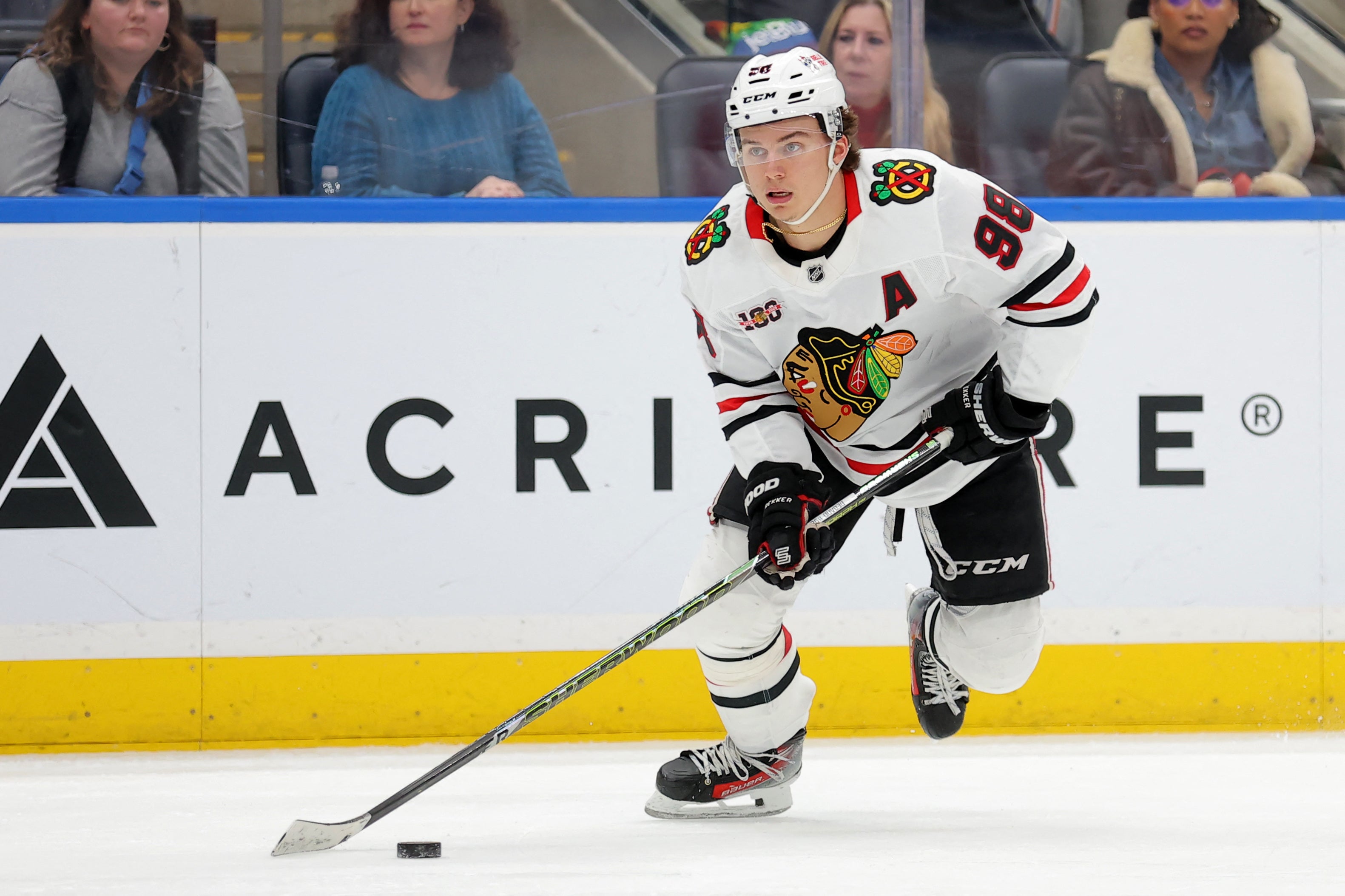 Ishockeyspelare i vit Blackhawks-tröja spelar med pucken på isen under en match.