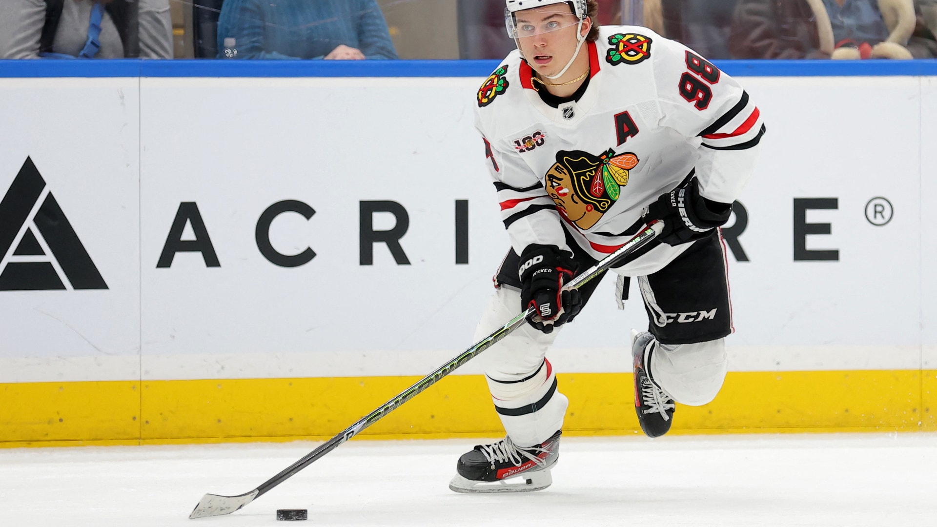 Ishockeyspelare i vit Blackhawks-tröja spelar med pucken på isen under en match.