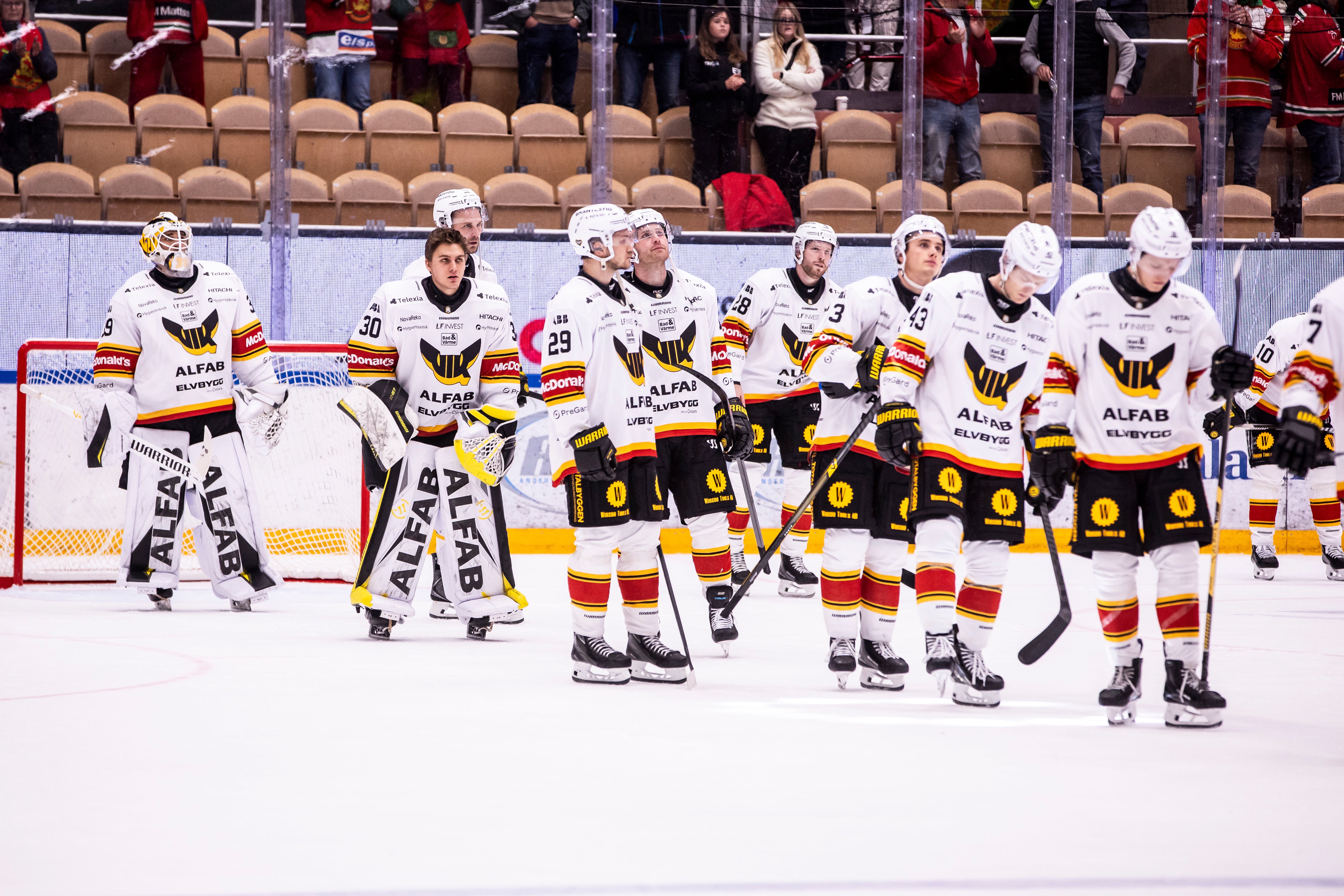 Hockeyspelare i vita matchtröjor står uppställda på rad på isen efter en match.