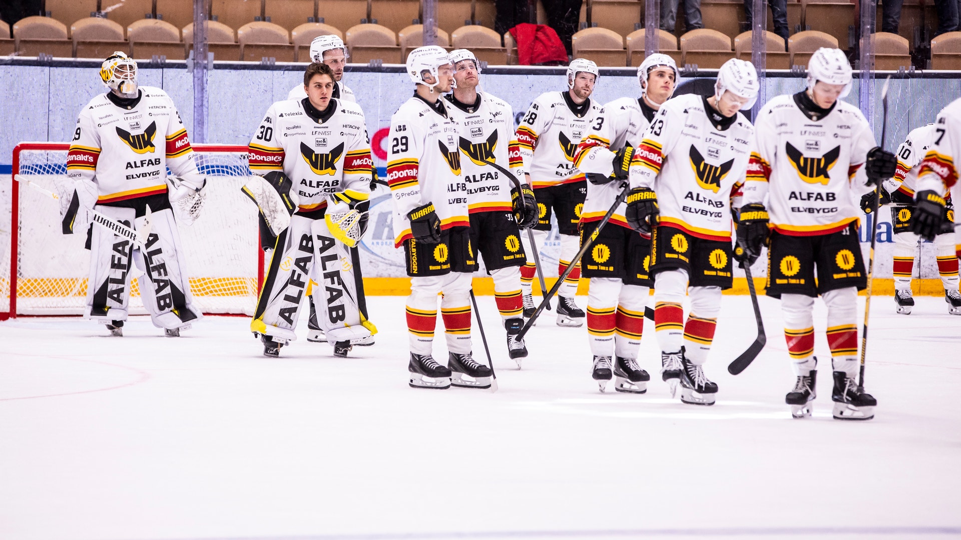 Hockeyspelare i vita matchtröjor står uppställda på rad på isen efter en match.