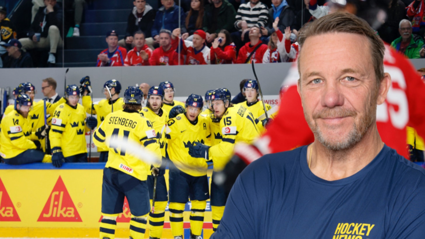 En man i mörkblå t-shirt med Hockey News-logga står framför ett ishockeylag i gul och blå utrustning som sitter på bänken.