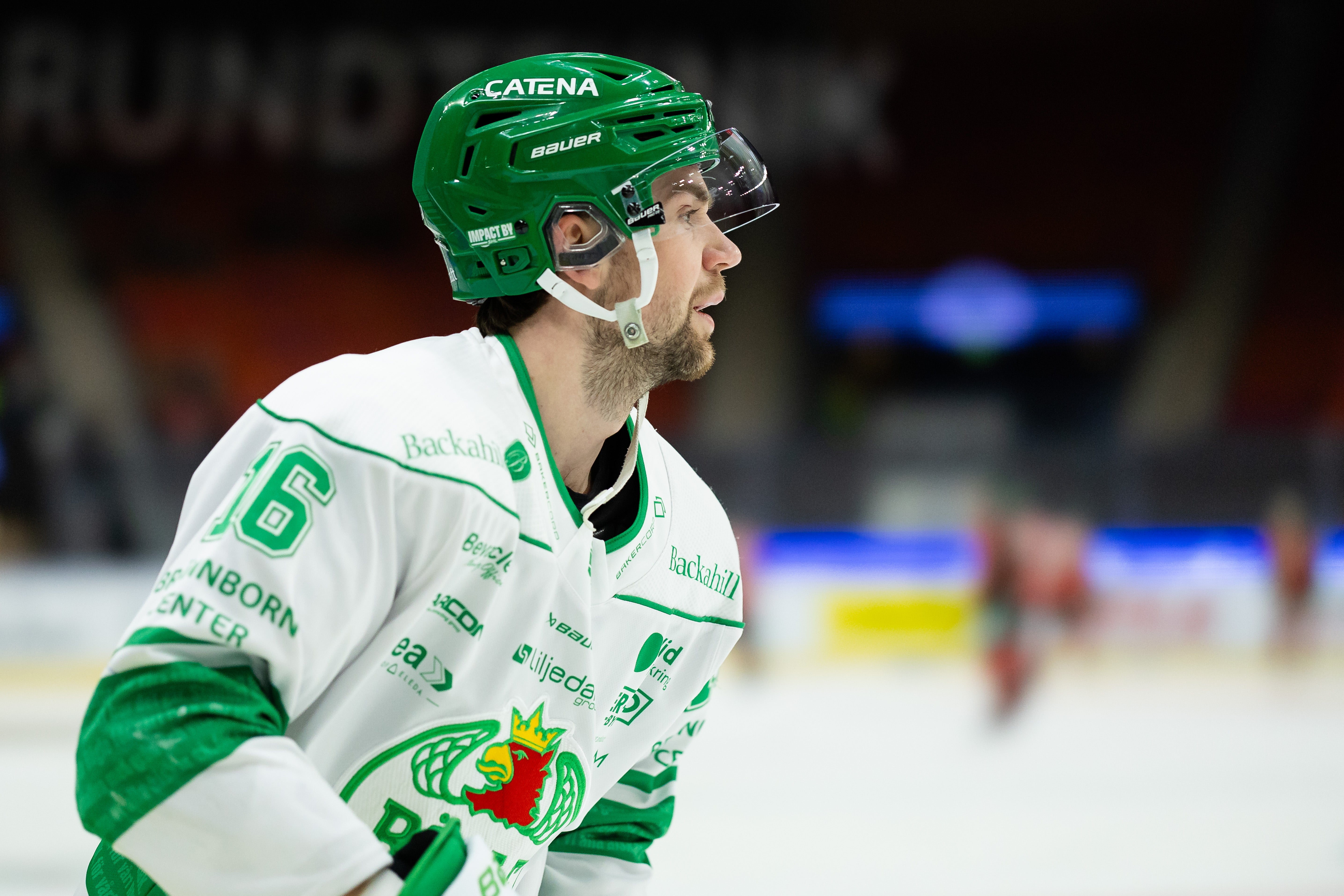 Ishockeyspelare i grön och vit lagdräkt med nummer 6 på isen under en match. Spelaren bär grön hjälm och ser fokuserad ut.