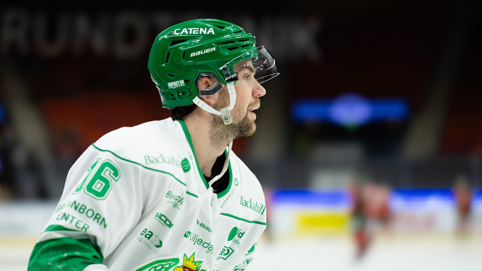 Ishockeyspelare i grön och vit lagdräkt med nummer 6 på isen under en match. Spelaren bär grön hjälm och ser fokuserad ut.