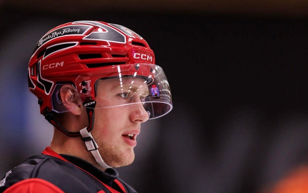 En ishockeyspelare i röd hjälm och matchtröja syns i profil på isen.