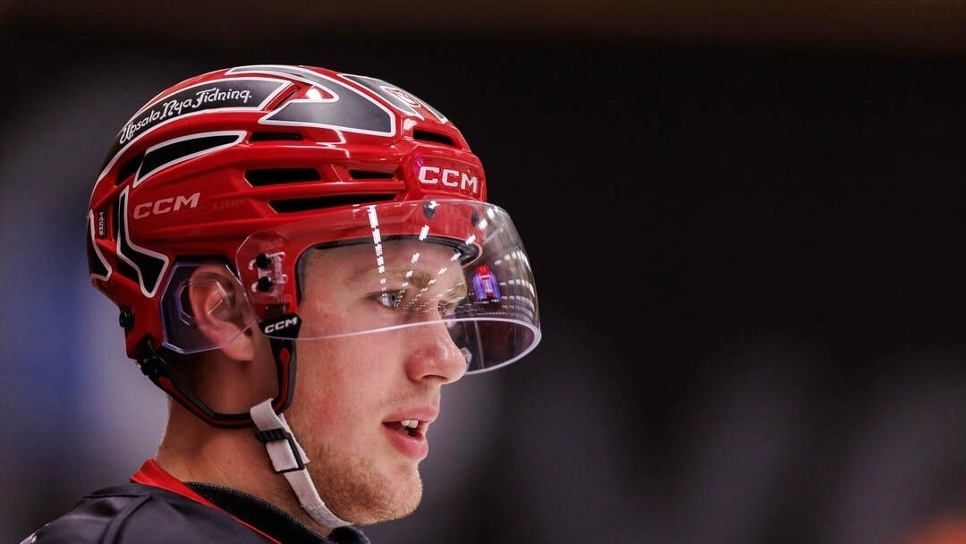 En ishockeyspelare i röd hjälm och matchtröja syns i profil på isen.