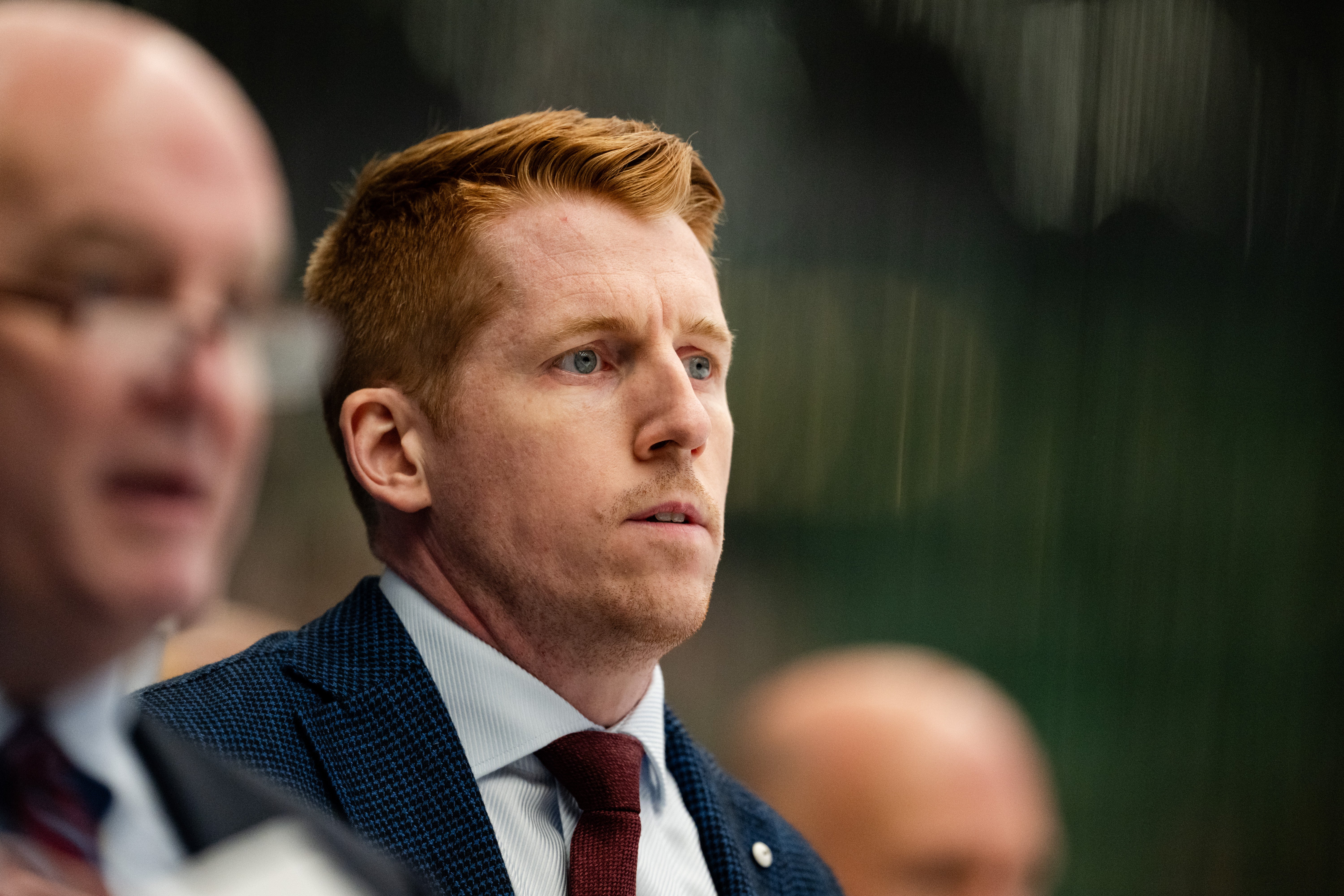 Porträtt av en man i mörkblå kostym och röd slips i en formell miljö.