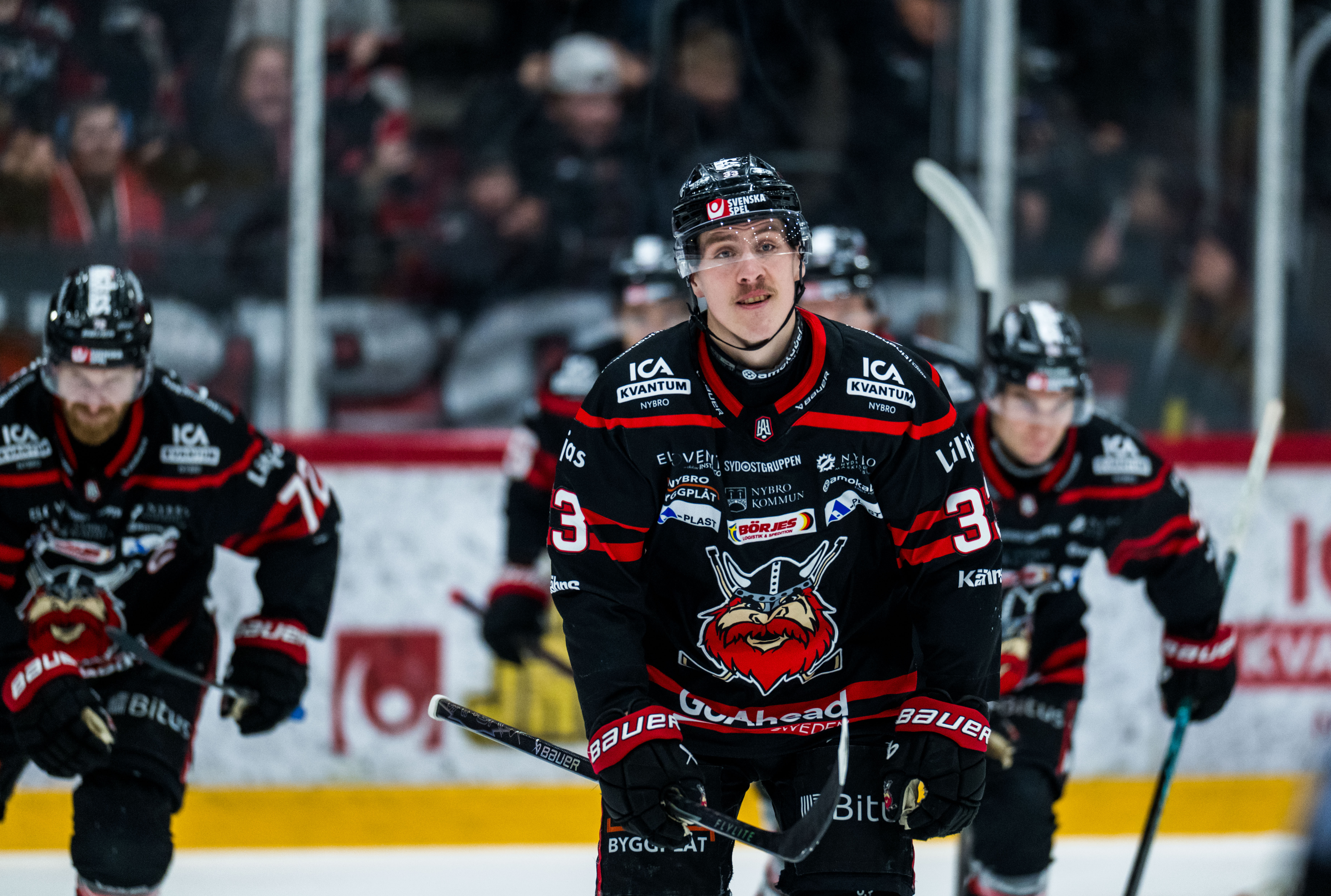 Tre ishockeyspelare i svarta tröjor med röda detaljer under en match på isen.