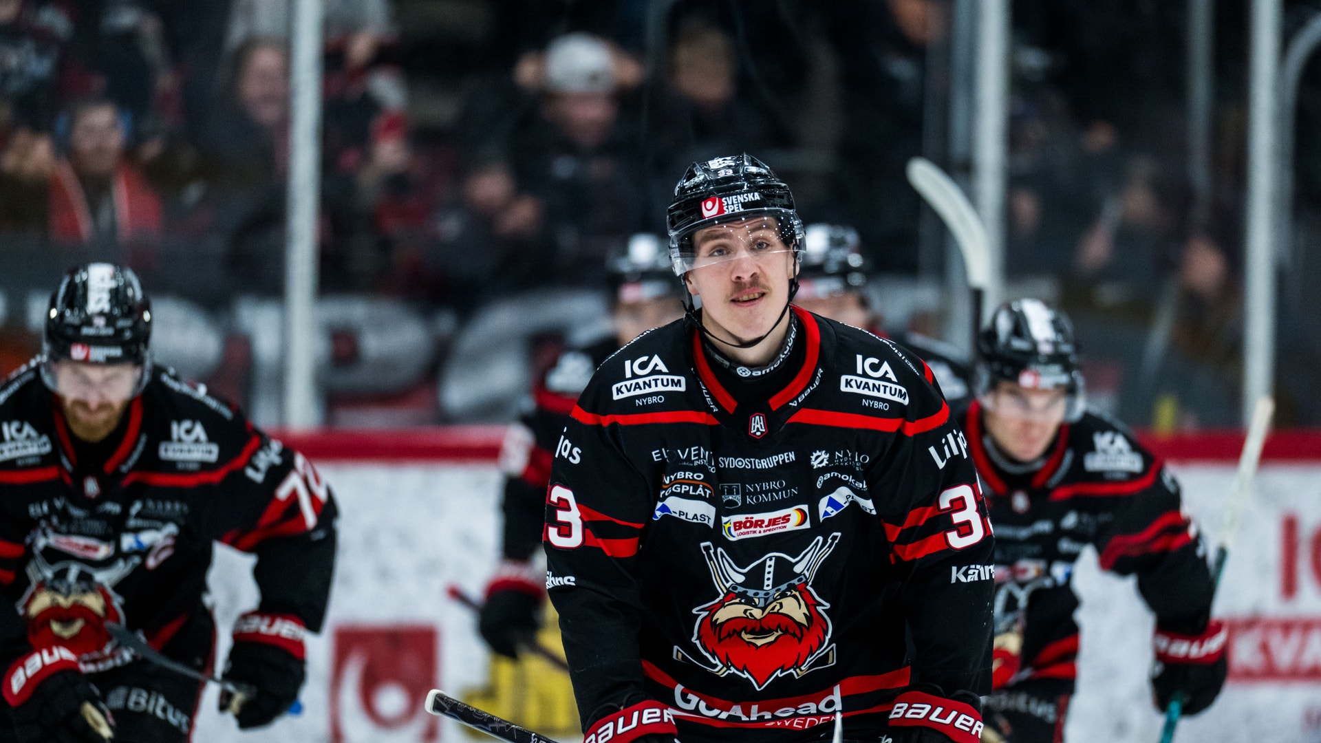 Tre ishockeyspelare i svarta tröjor med röda detaljer under en match på isen.