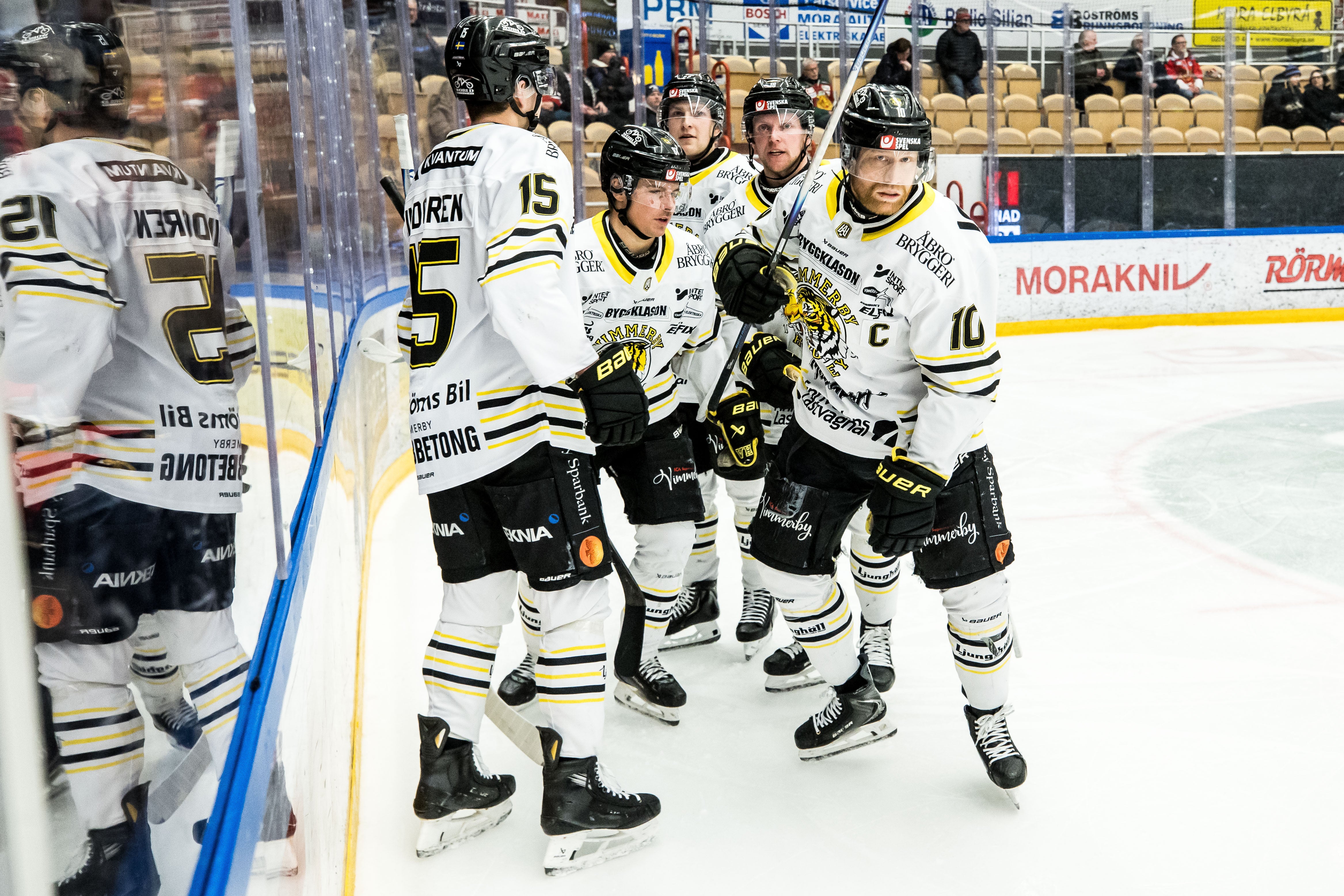 Ishockeyspelare i vita och svarta trikåer samlas vid borden under en match.