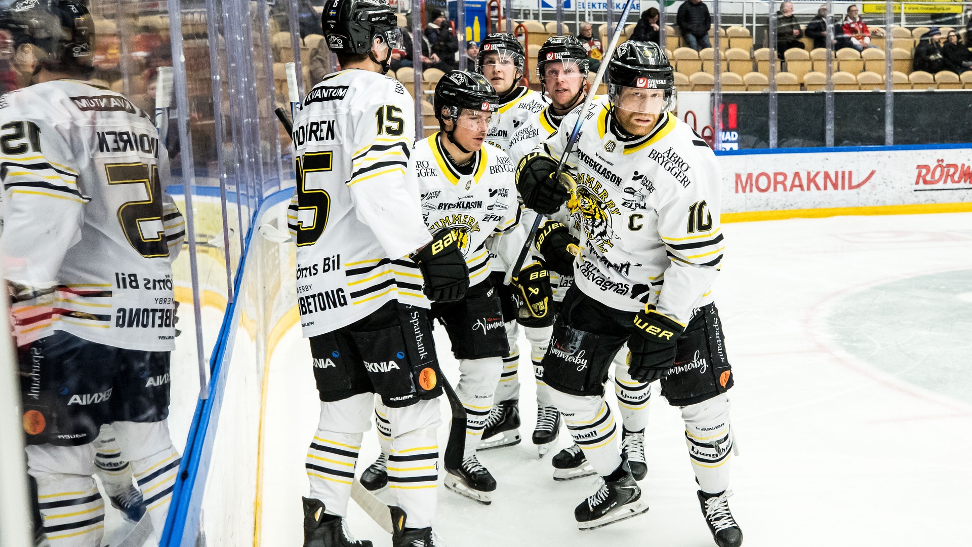 Ishockeyspelare i vita och svarta trikåer samlas vid borden under en match.