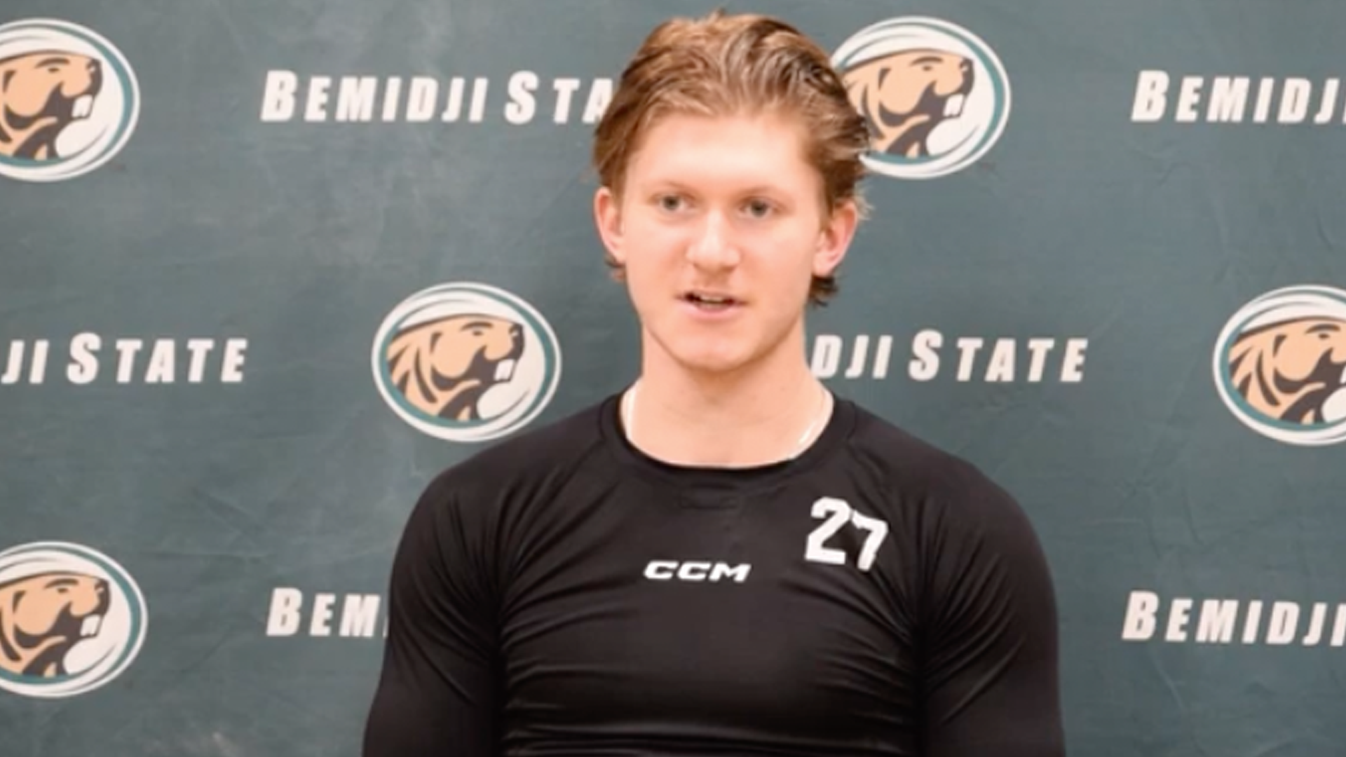 Porträtt av en ung ishockeyspelare i svart CCM-tröja med nummer 27, framför en Bemidji State-bakgrund.