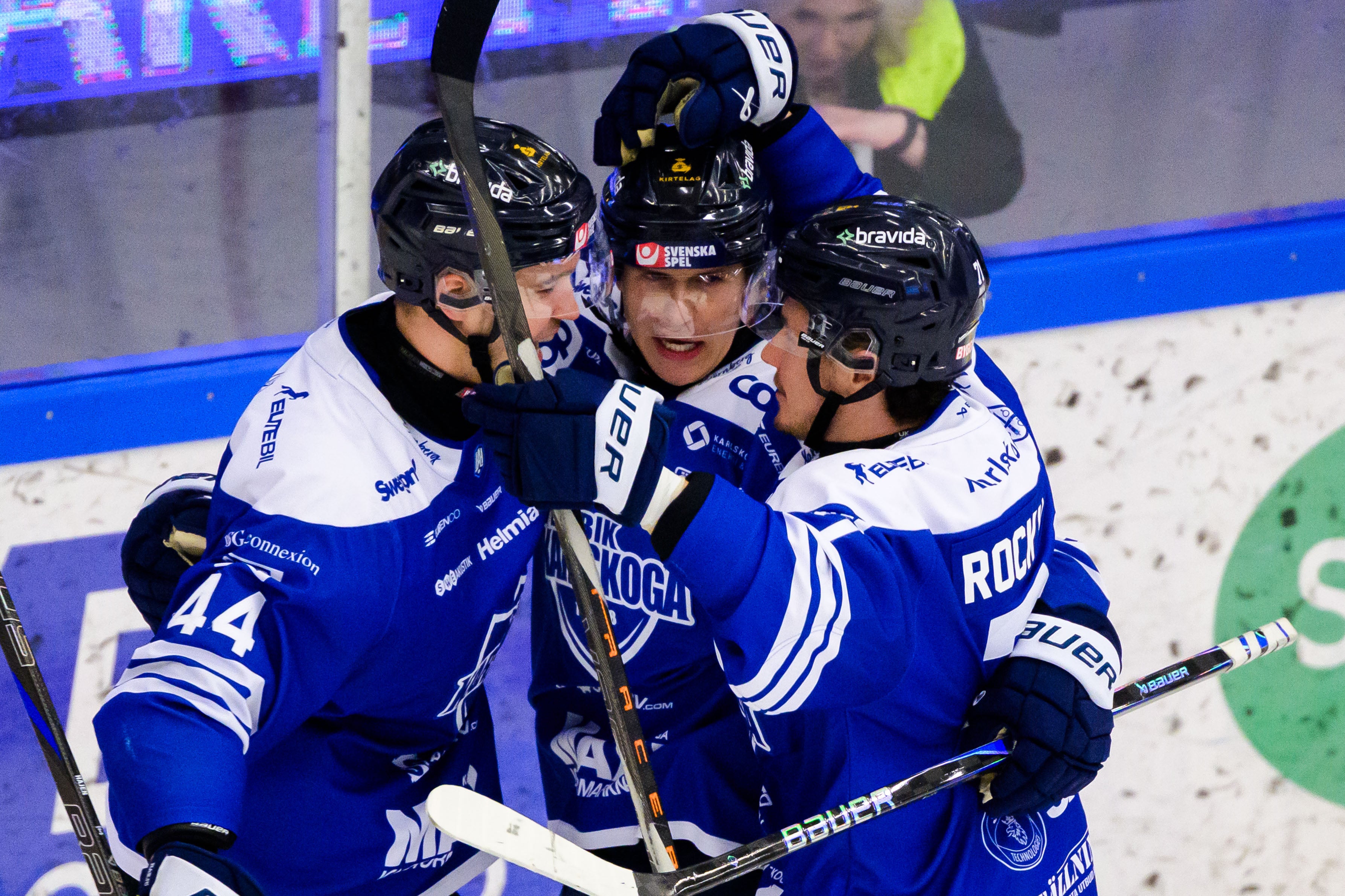 Fyra ishockeyspelare i blå och vita tröjor jublar tillsammans på isen under en match.