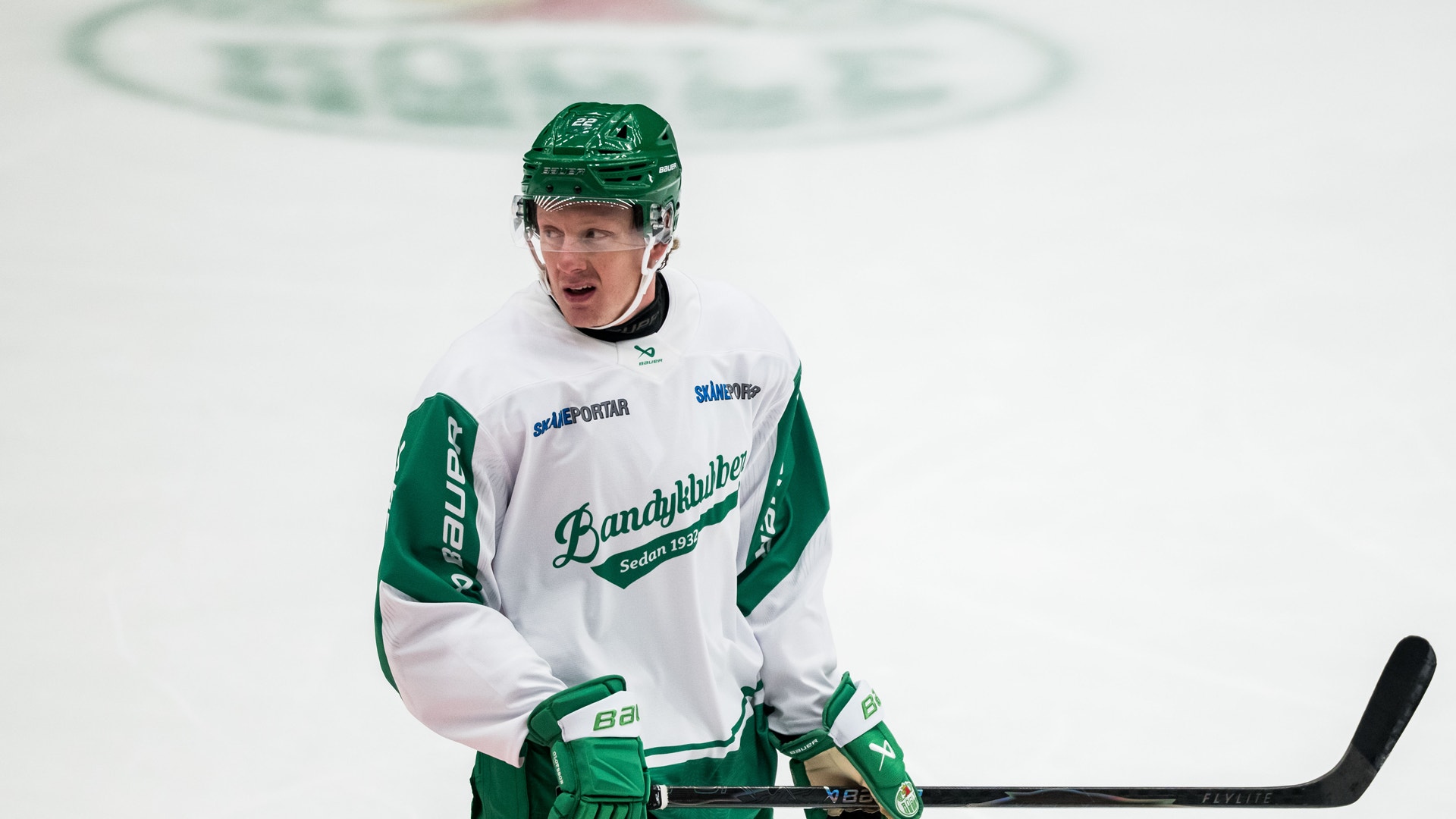 Ishockeyspelare i grön och vit matchdräkt med hjälm och ishockeyklubbor på isen.
