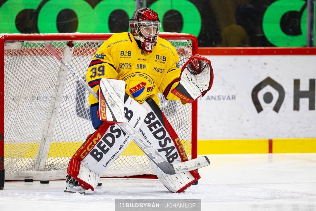 Ishockeymålvakt i gul och röd utrustning i skyddande position framför målet under en match.