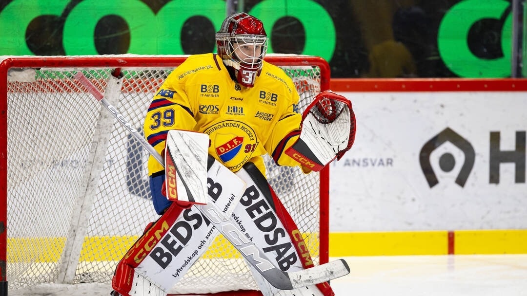 Ishockeymålvakt i gul och röd utrustning i skyddande position framför målet under en match.