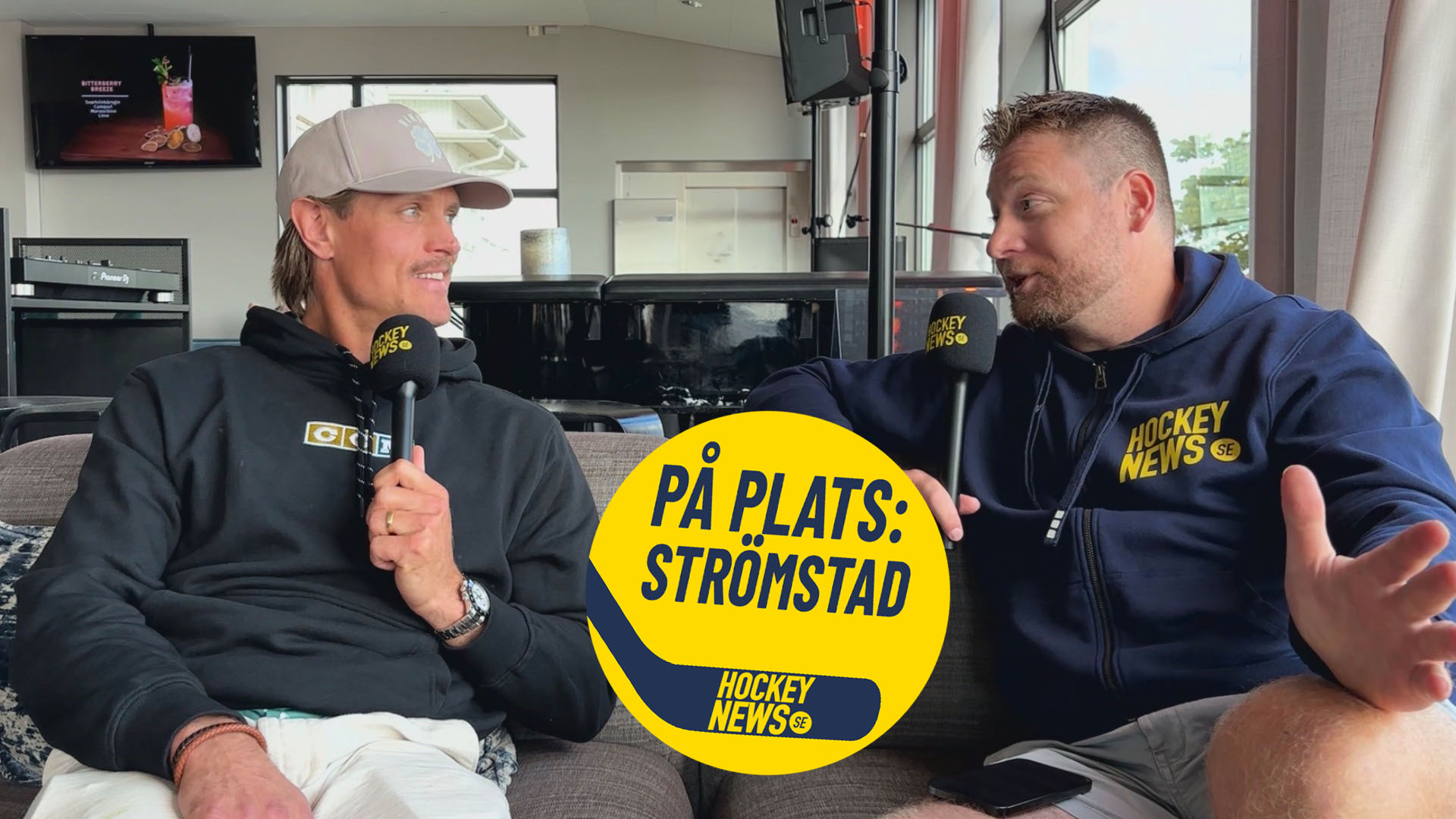 Två män sitter och samtalar i en studio. De håller en gul skylt med texten "PÅ PLATS: STRÖMSTAD" och bär båda kläder märkta med Hockey News-logotypen.