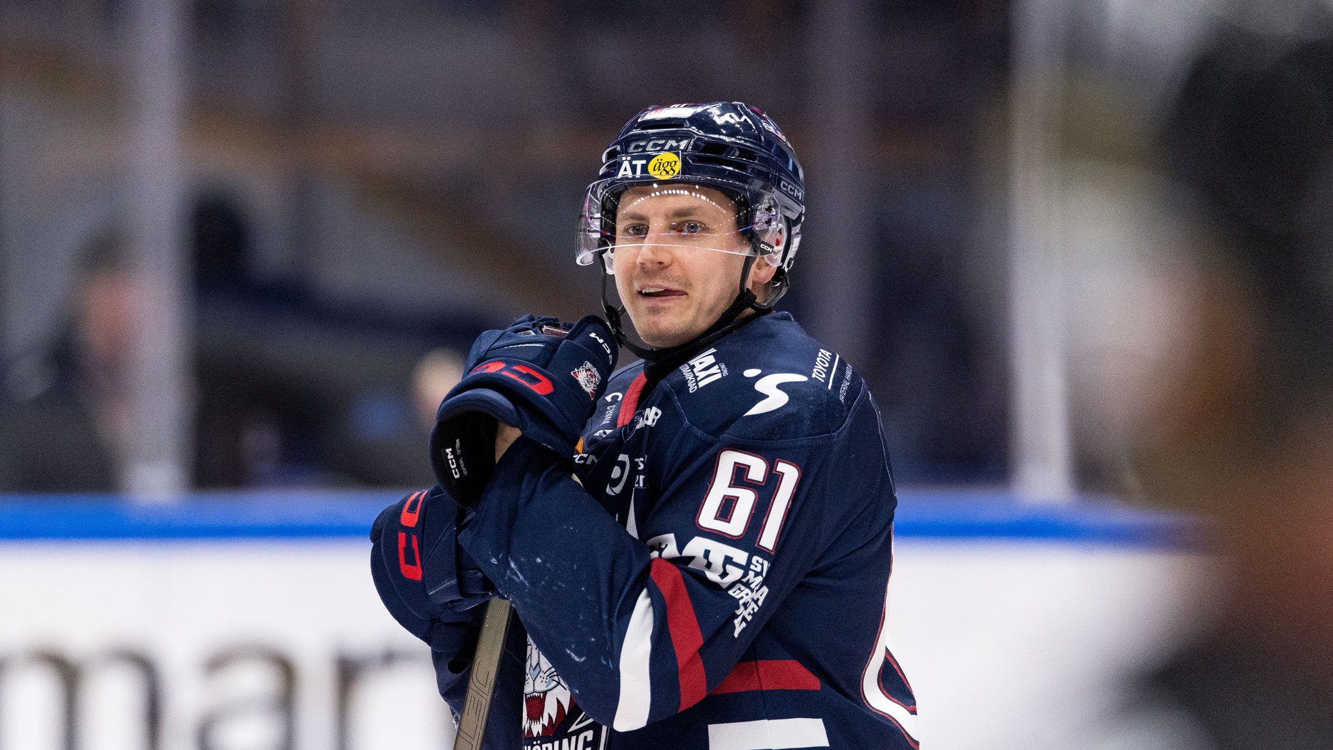 Ishockeyspelare i mörkblå matchdräkt med nummer 61 står på isen under en match.