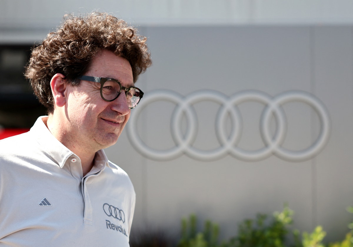 Porträtt av en man med glasögon och lockigt brunt hår, klädd i vit Audi-skjorta framför Audi-logotyp.