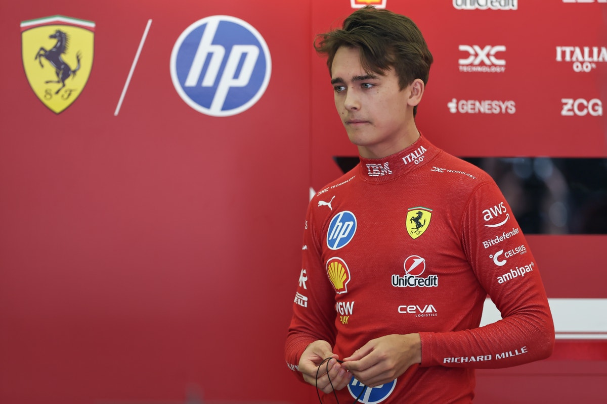 En Formel 1-förare i röd Ferrari-overall står framför en sponsorvägg med Ferrari- och HP-logotyper.