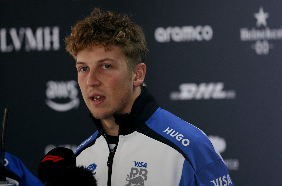 Porträttfoto av en ung man i blå och vit sportjacka vid en presskonferens.