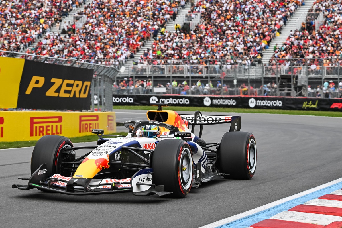 En Formel 1-bil i röd och blå färg kör på en racerbana framför en fullsatt läktare med åskådare.