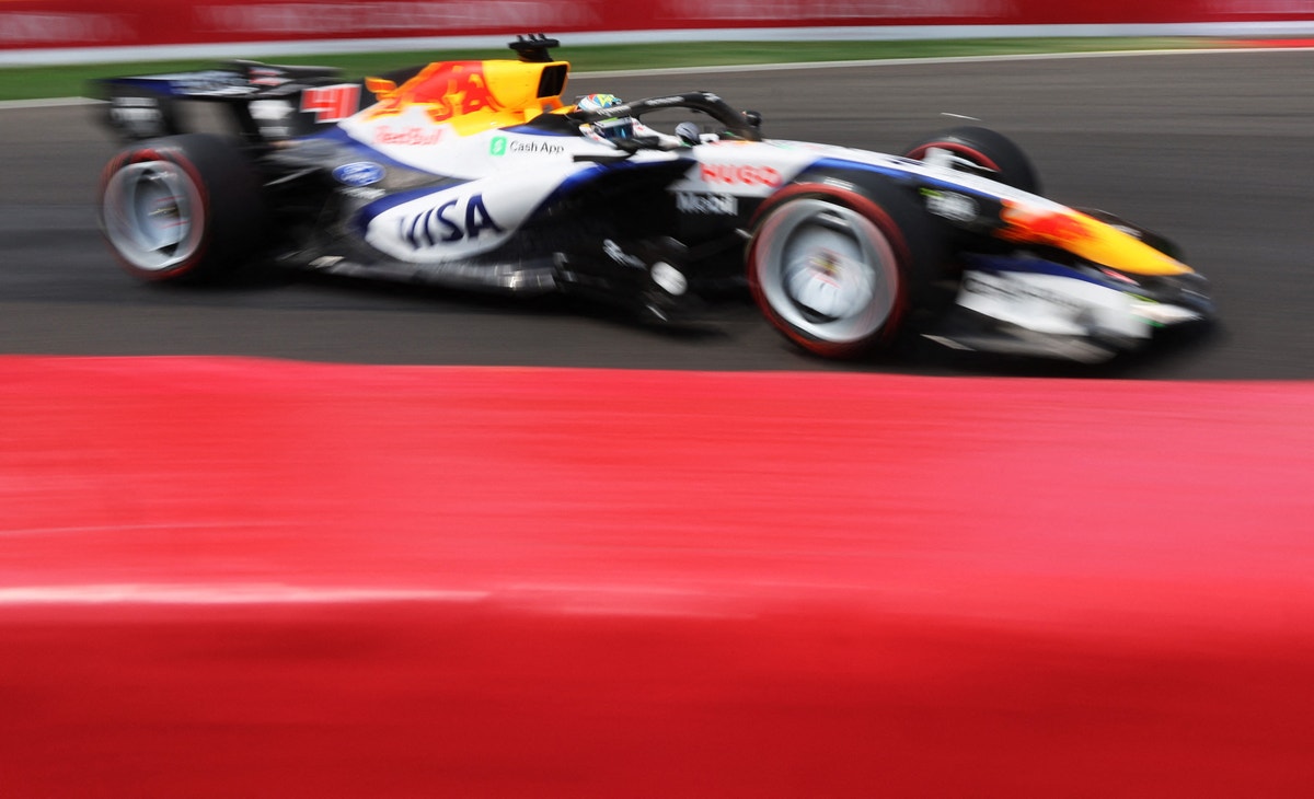 En formel 1-bil i röd och blå färg kör på en racerbana med höga hastigheter. Bilden visar rörelseoskärpa som ger en dynamisk känsla av farten.
