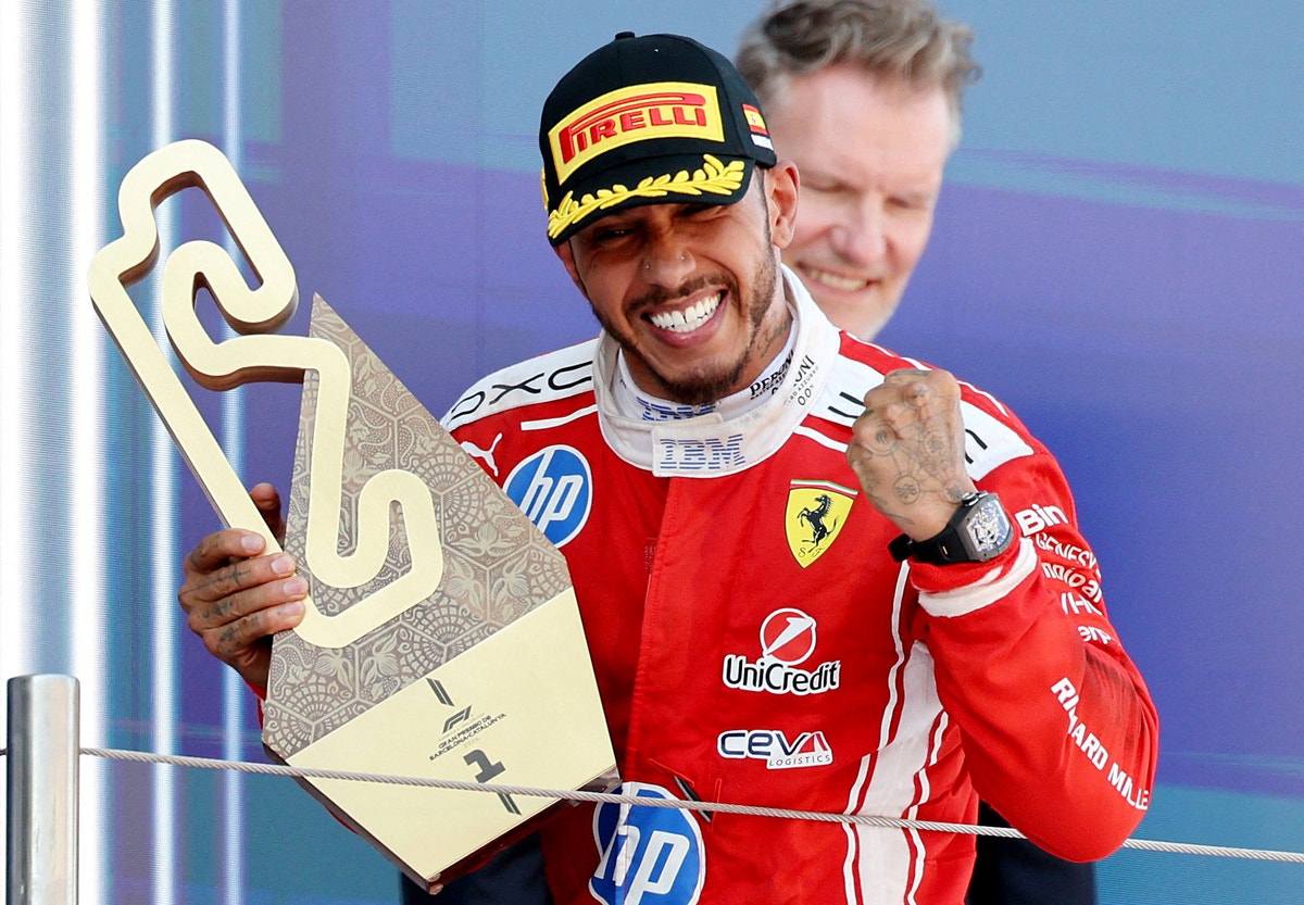 En Formel 1-förare i Ferrari-dräkt står på ett podium och håller i en trofé efter att ha vunnit ett lopp.