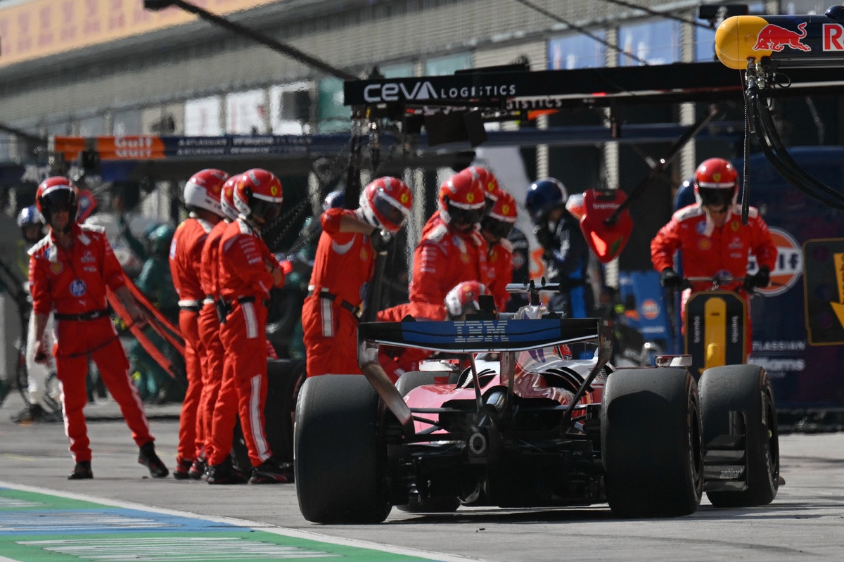 En röd Ferrari Formel 1-bil på depån under ett race, omgiven av teammedlemmar i röda overaller.